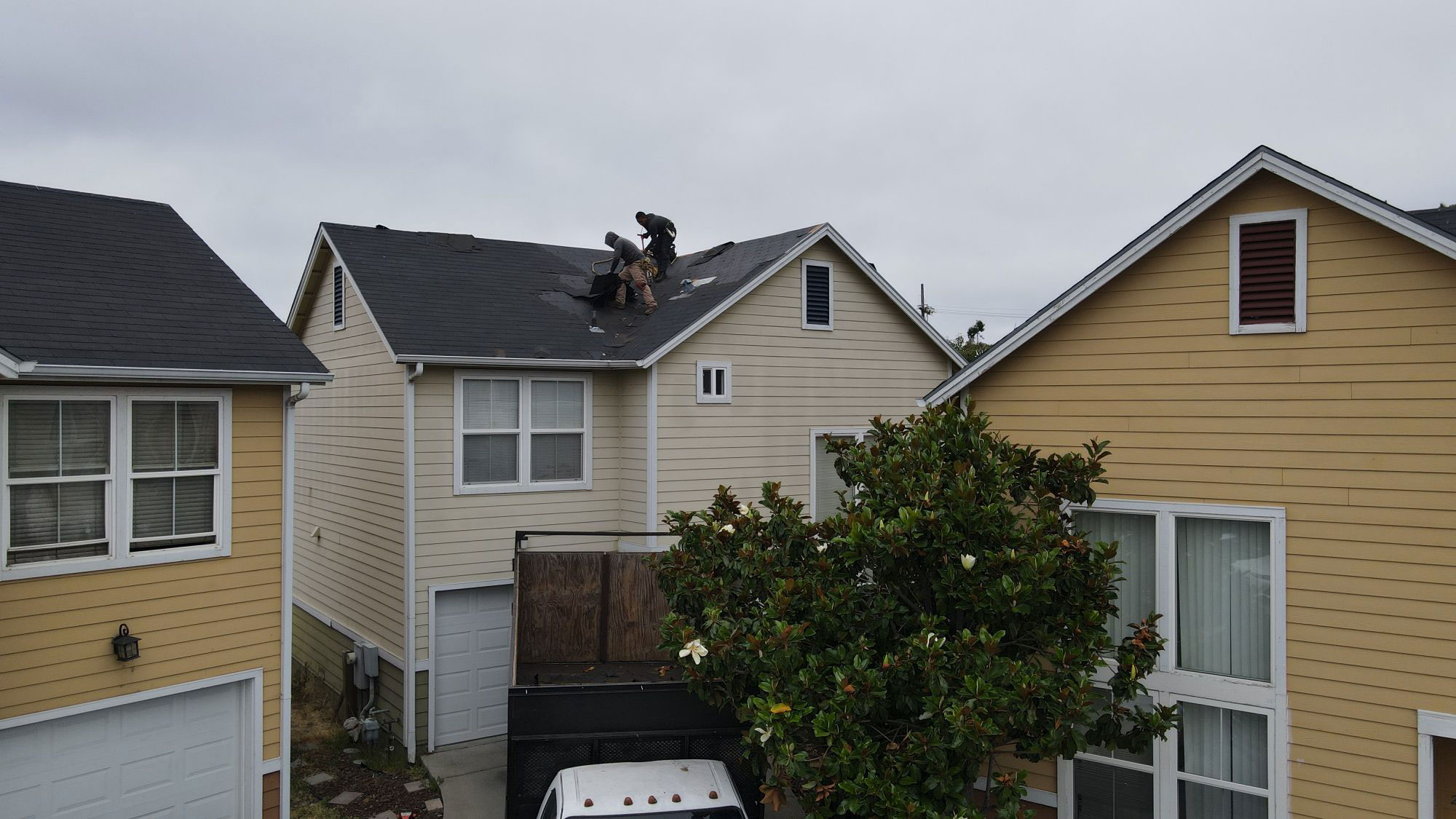 The image shows a residential area with two-story houses, one of which has a visible roof repair underway.