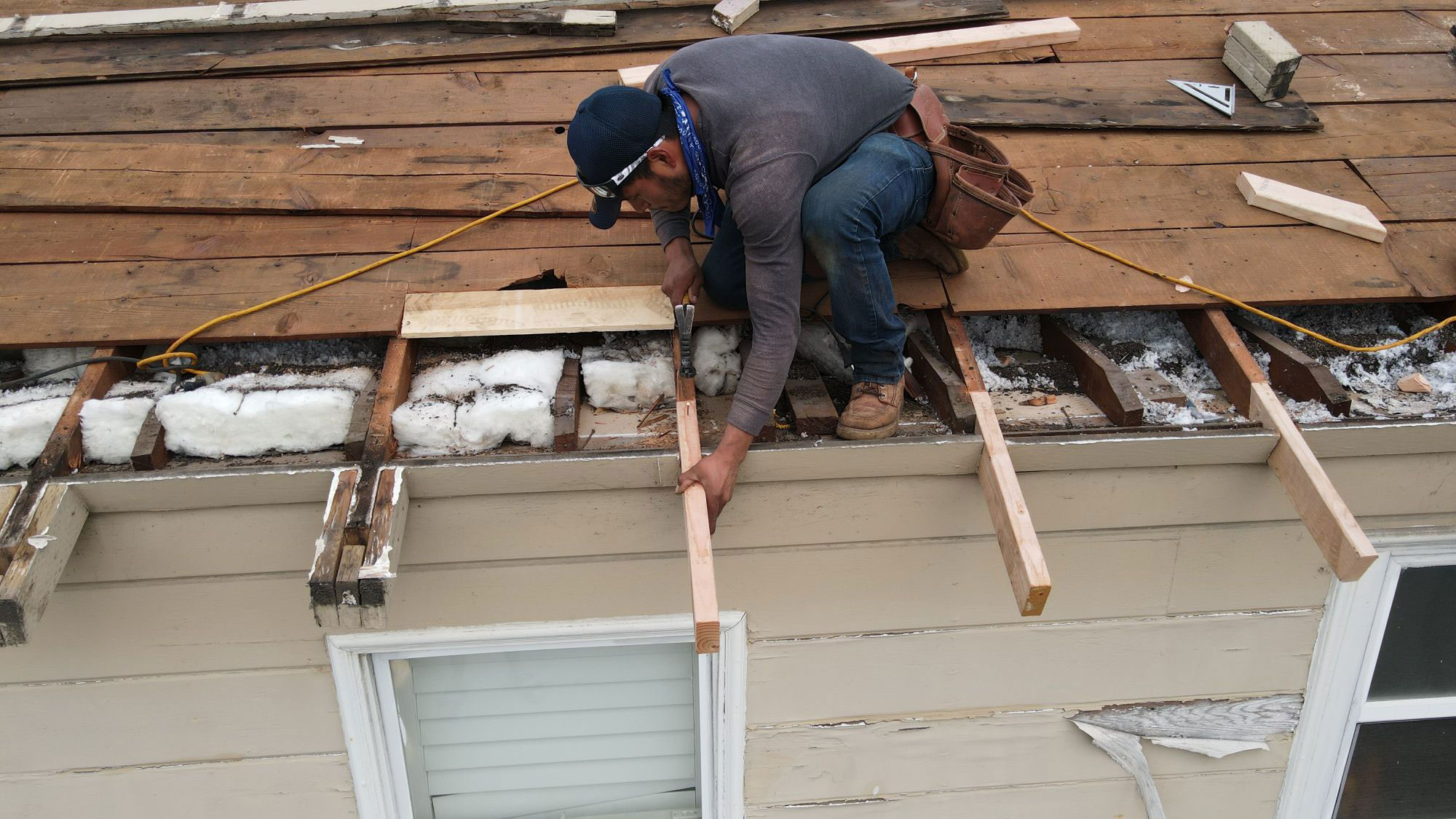 The image shows a person working on a roof repair, with visible tools and materials indicating ongoing construction or renovation activity.