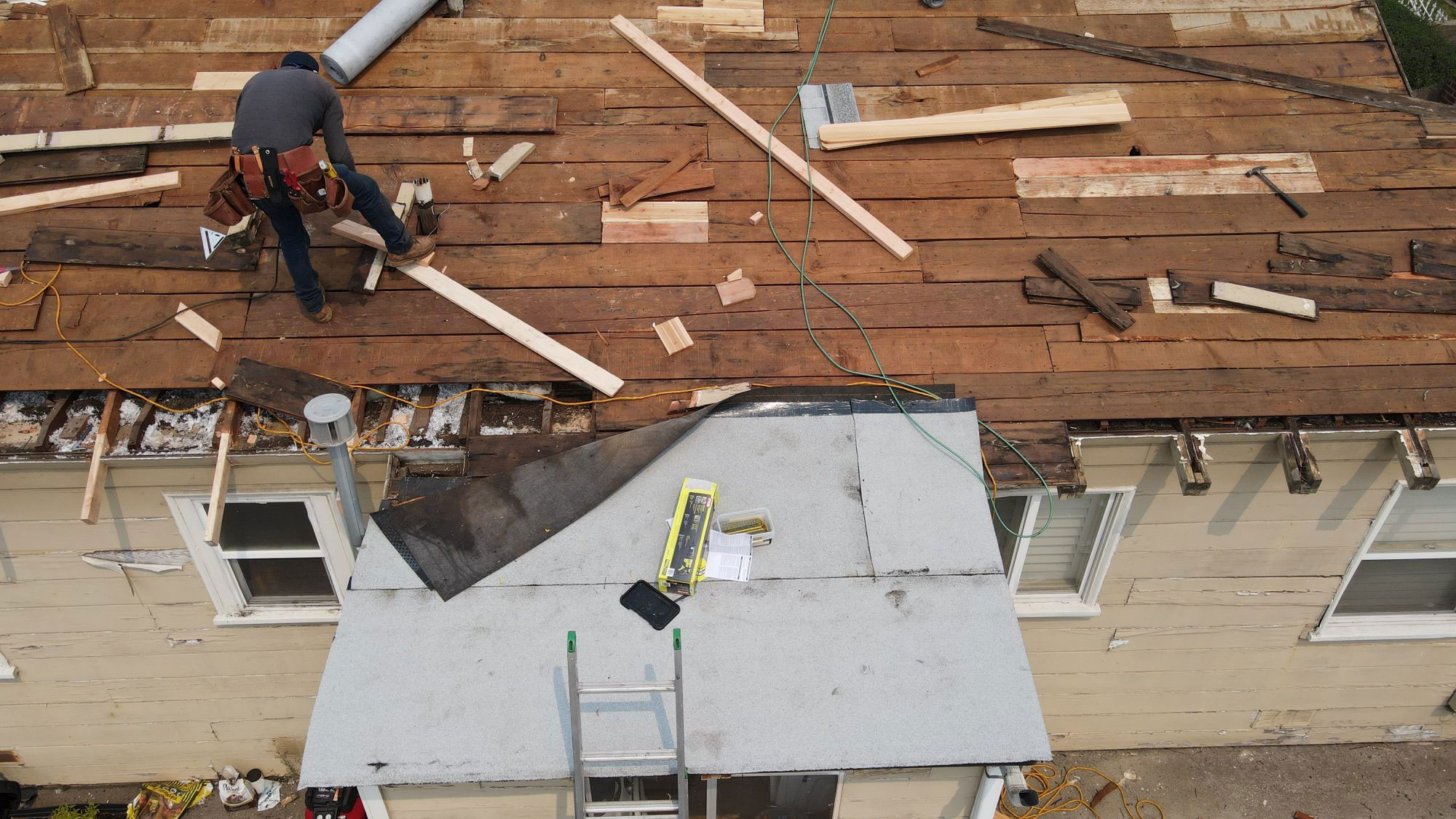 A person working on a roof repair with plywood, nails, and other materials scattered around.