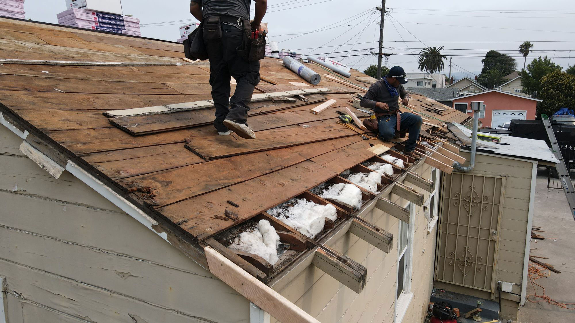 A person working on a roof repair with shingles missing, standing on a partially completed structure.