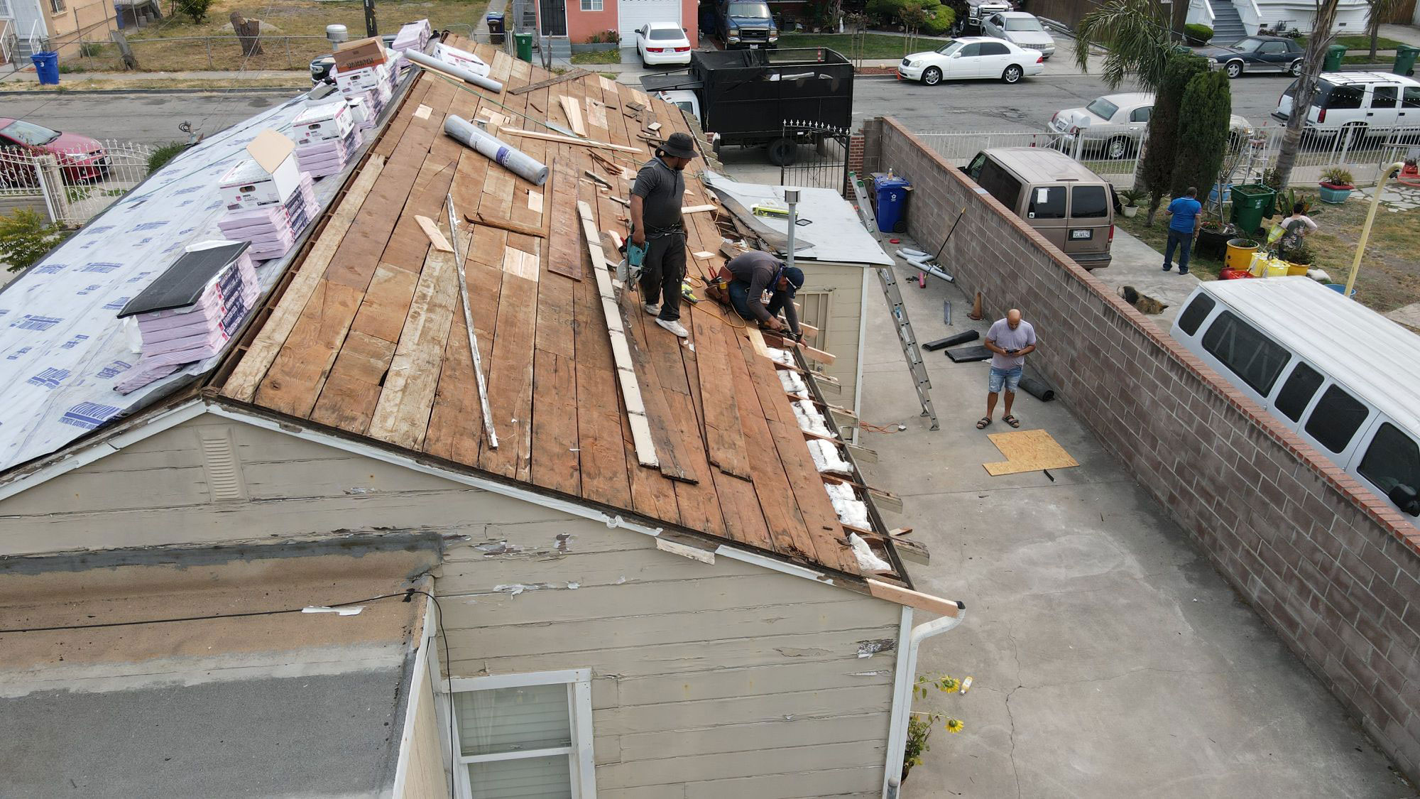 The image shows a roofing project underway with workers on the roof and construction materials visible.