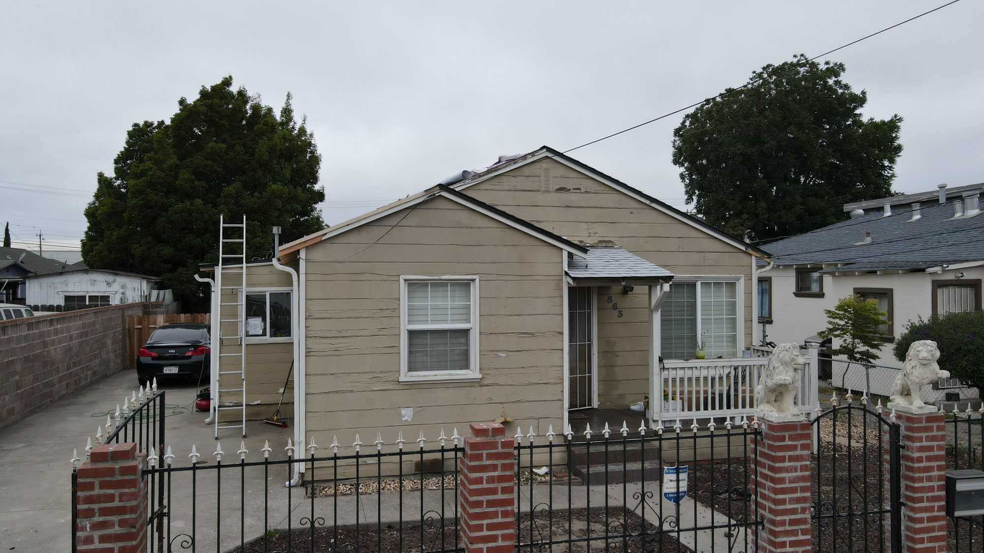 The image shows a single-story house with a visible foundation, a white fence, and a front yard with a driveway. It appears to be a residential property with a fenced backyard.