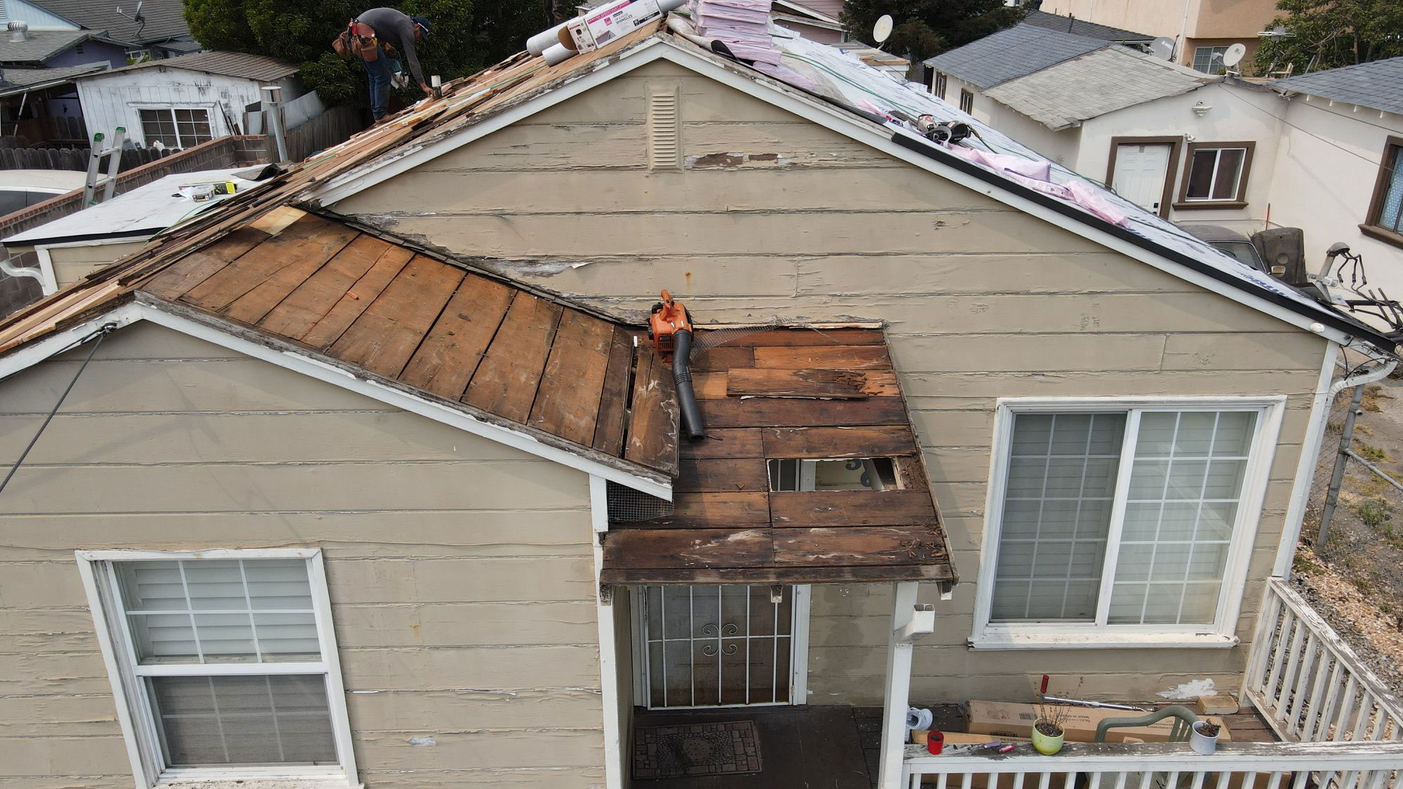 The image shows a house with a damaged roof under repair, featuring visible shingles and a person working on the structure.