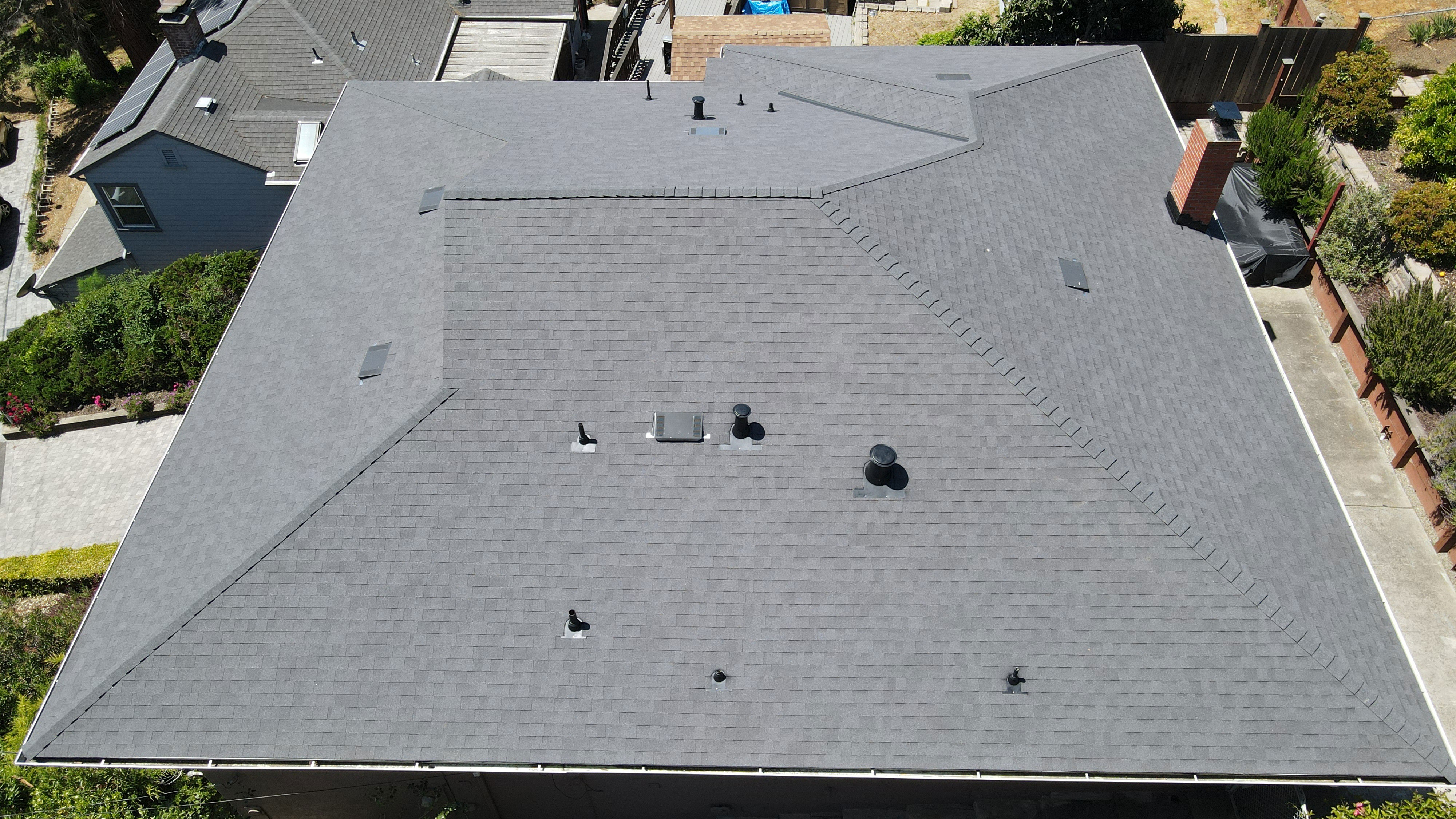 The image shows a residential house with a gray shingle roof, featuring multiple sloped sections and a prominent triangular skylight on the left side.