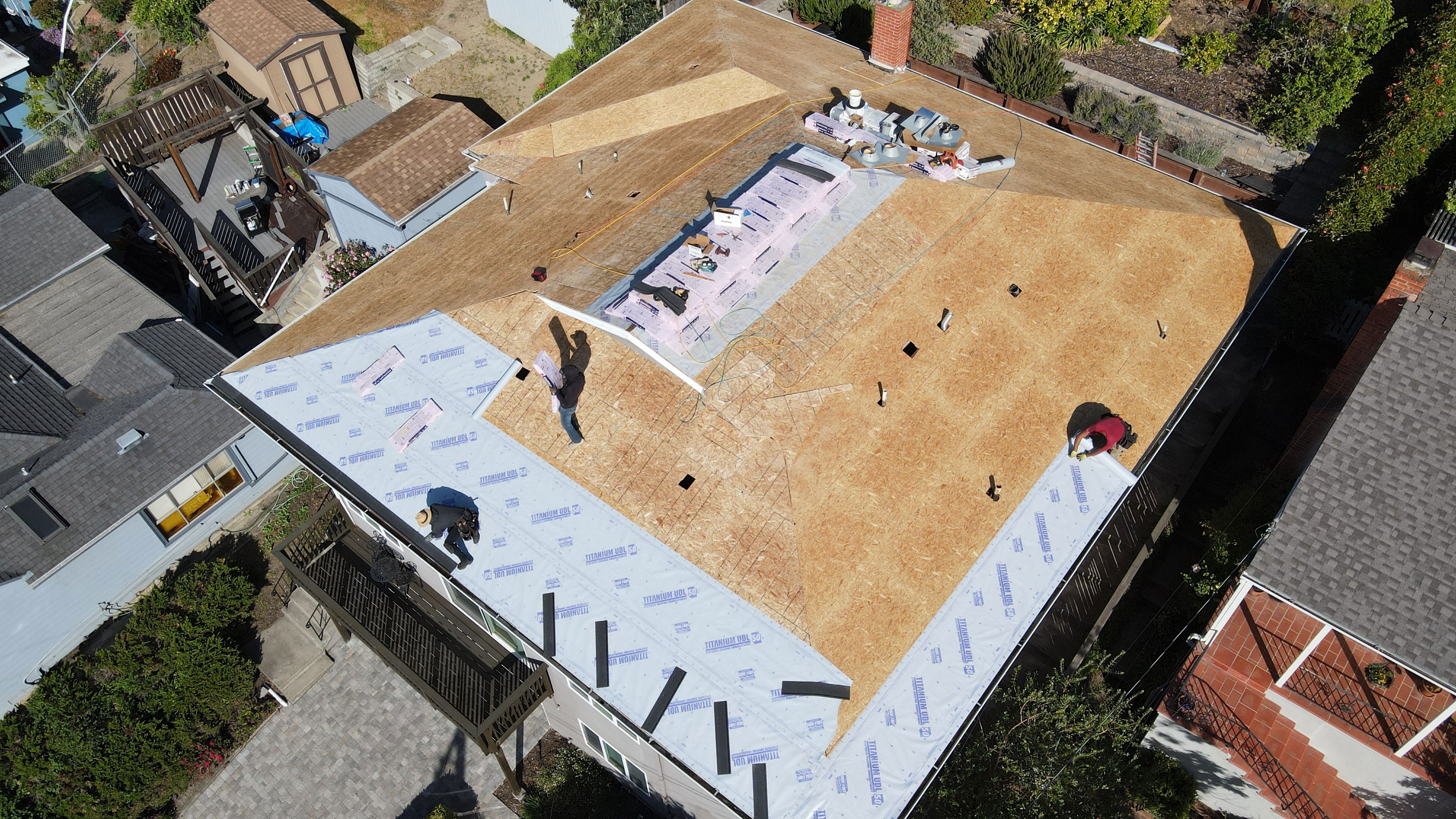 The image shows a roof under construction with various materials and tools visible, indicating an ongoing renovation or repair project.