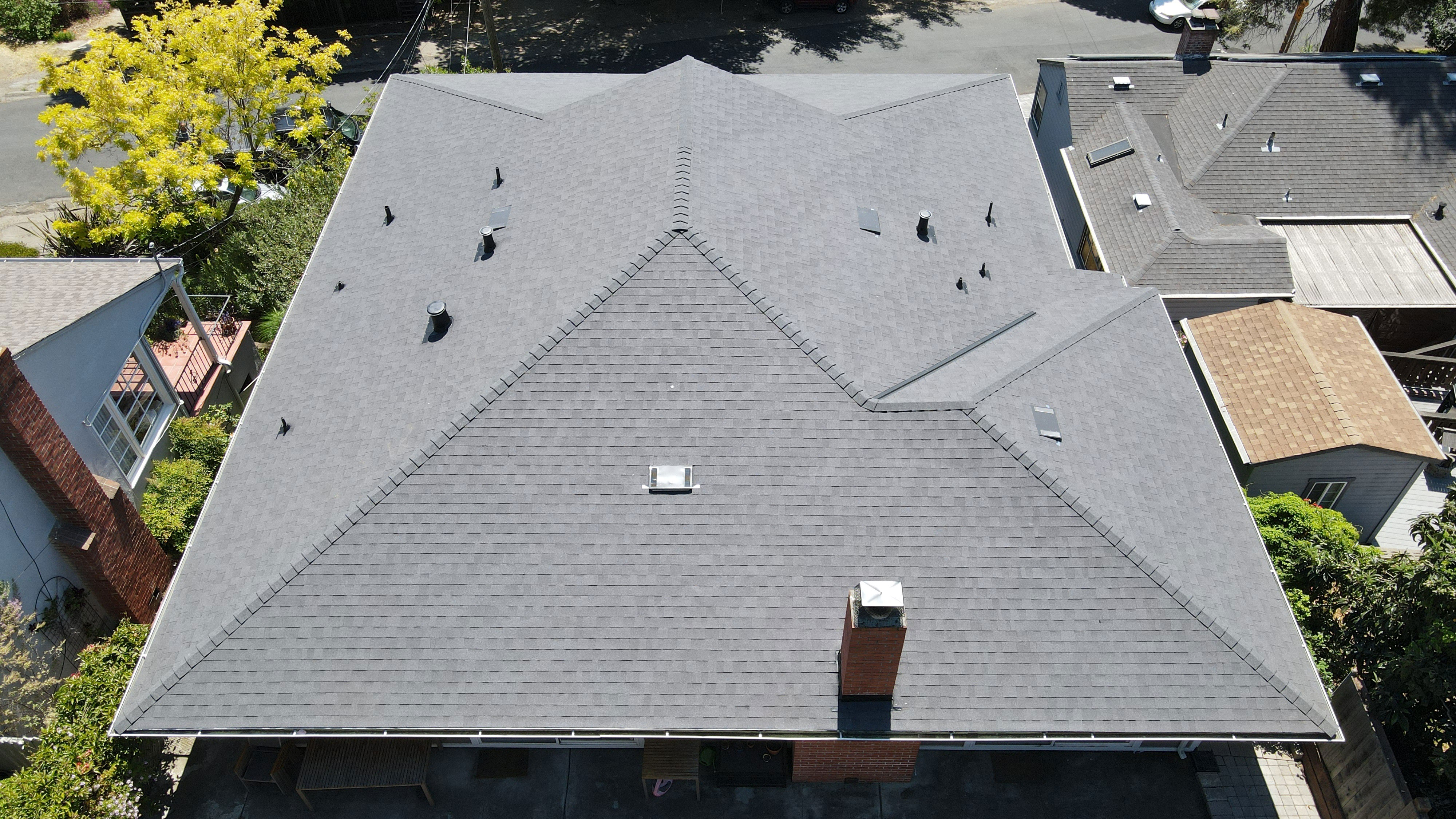 A single-story residential building with a dark gray shingled roof under a clear sky.