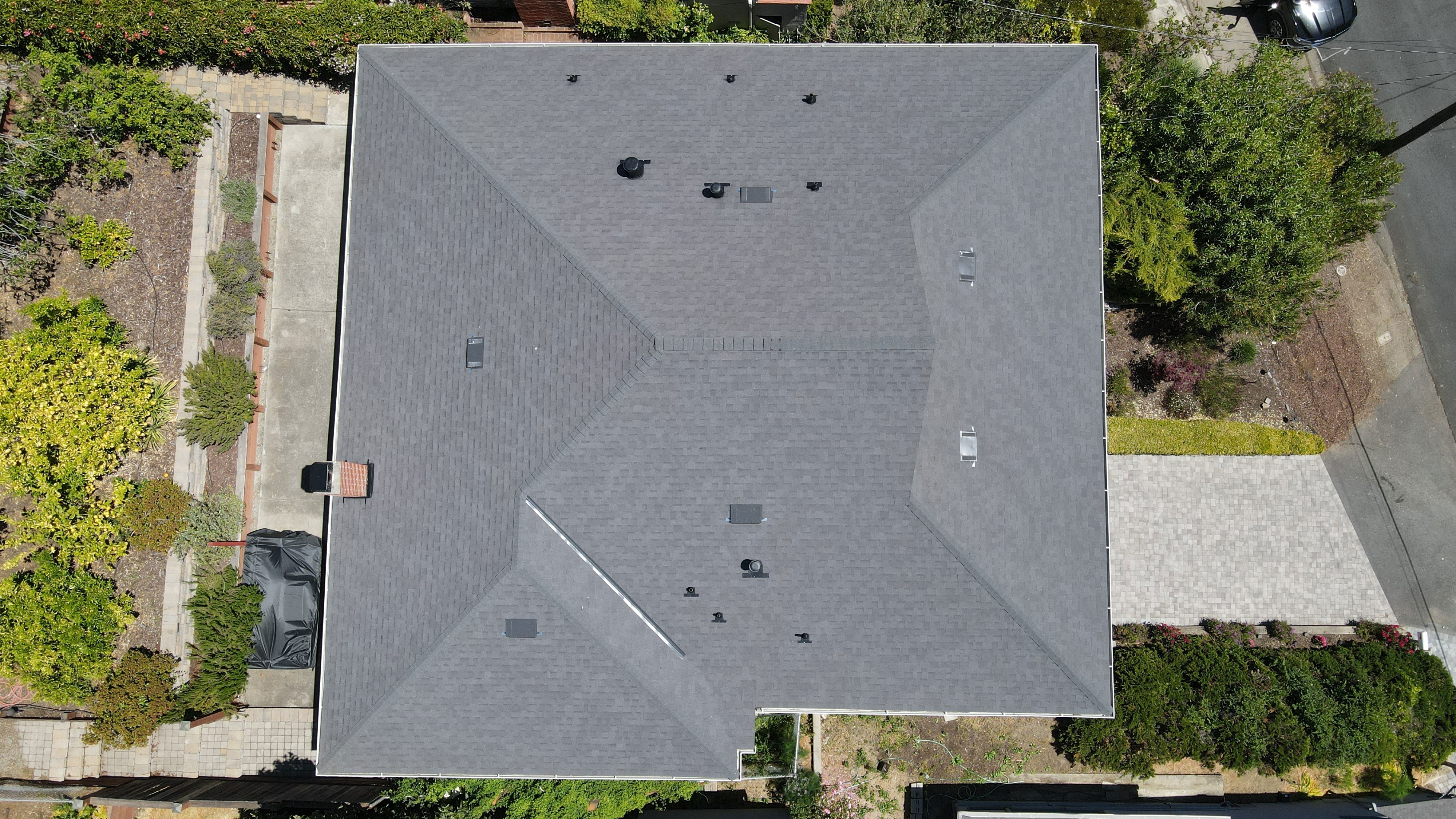 An aerial view of a residential house with a grey shingled roof and a flat front yard.