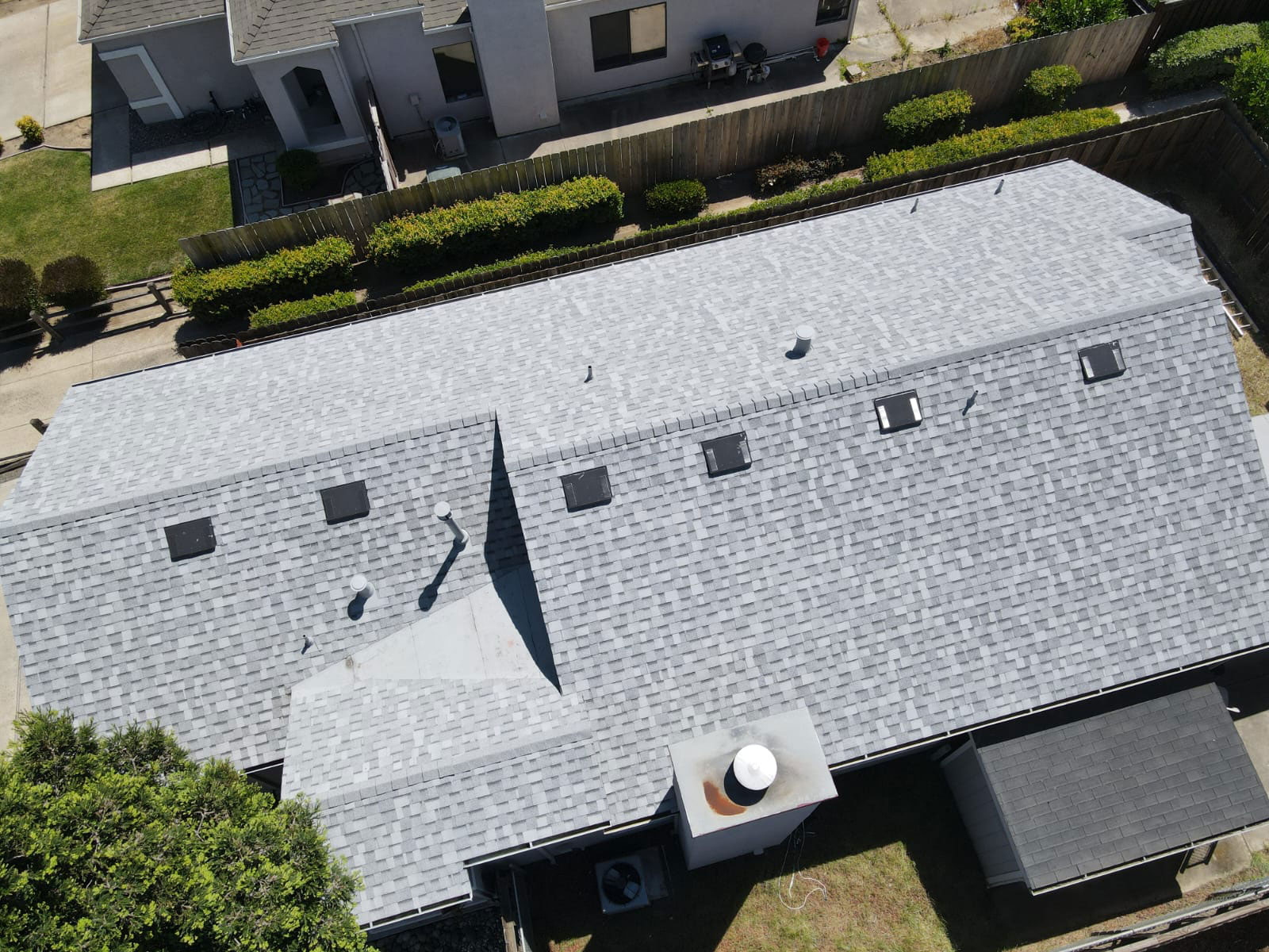 The image shows a house with a gray shingle roof, featuring multiple windows and a chimney. There is a white vent pipe visible on the roof. The house appears to be a single-family dwelling with a garage attached at the rear.