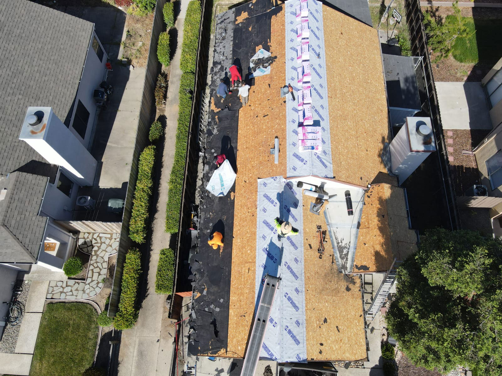 The image shows a house undergoing roof construction with workers on scaffolding, and it appears to be taken from an elevated perspective, possibly from another building across the street.