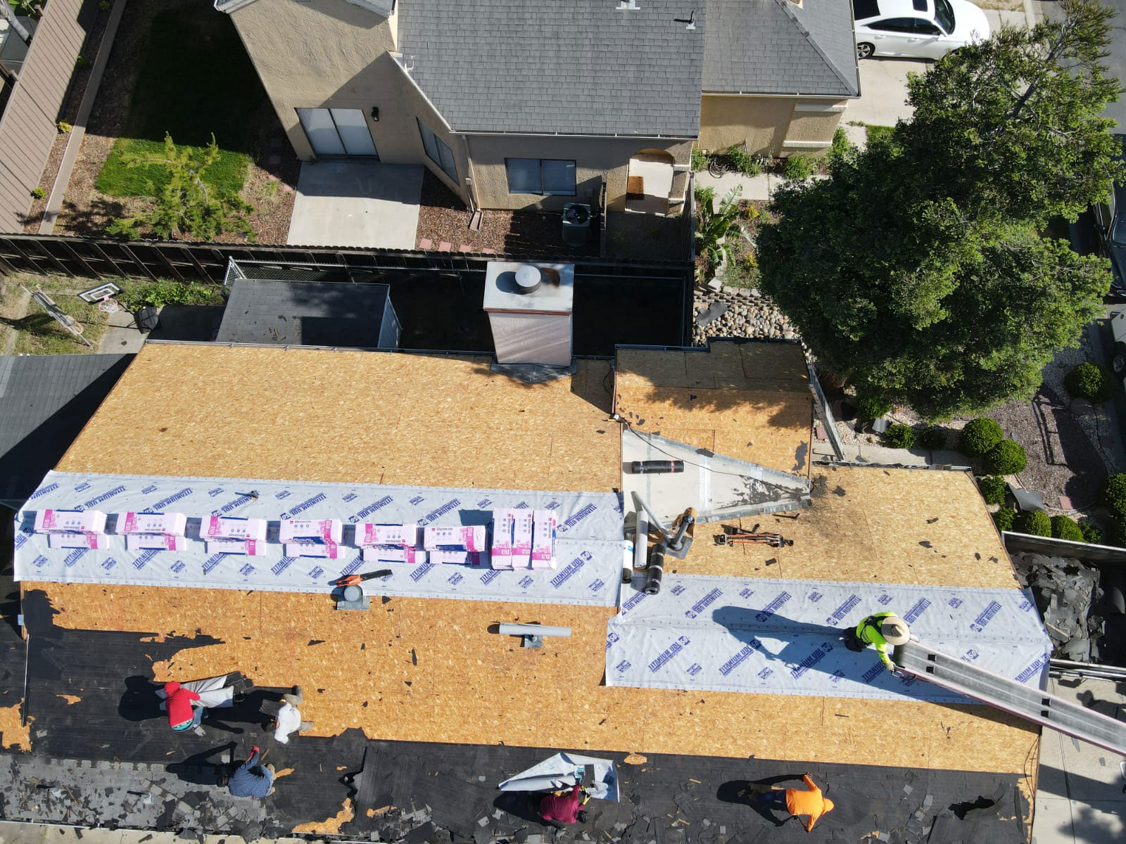 The image shows a residential building under construction with visible roofing materials and workers on site.