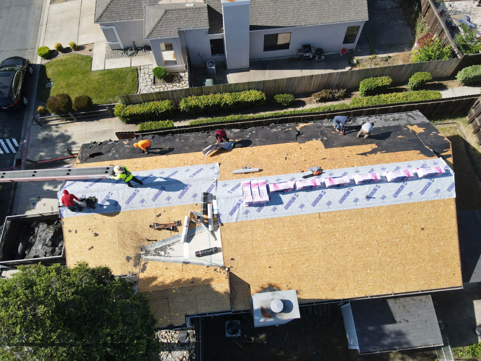 The image shows a construction site with workers on a roof undergoing renovation or repair work.