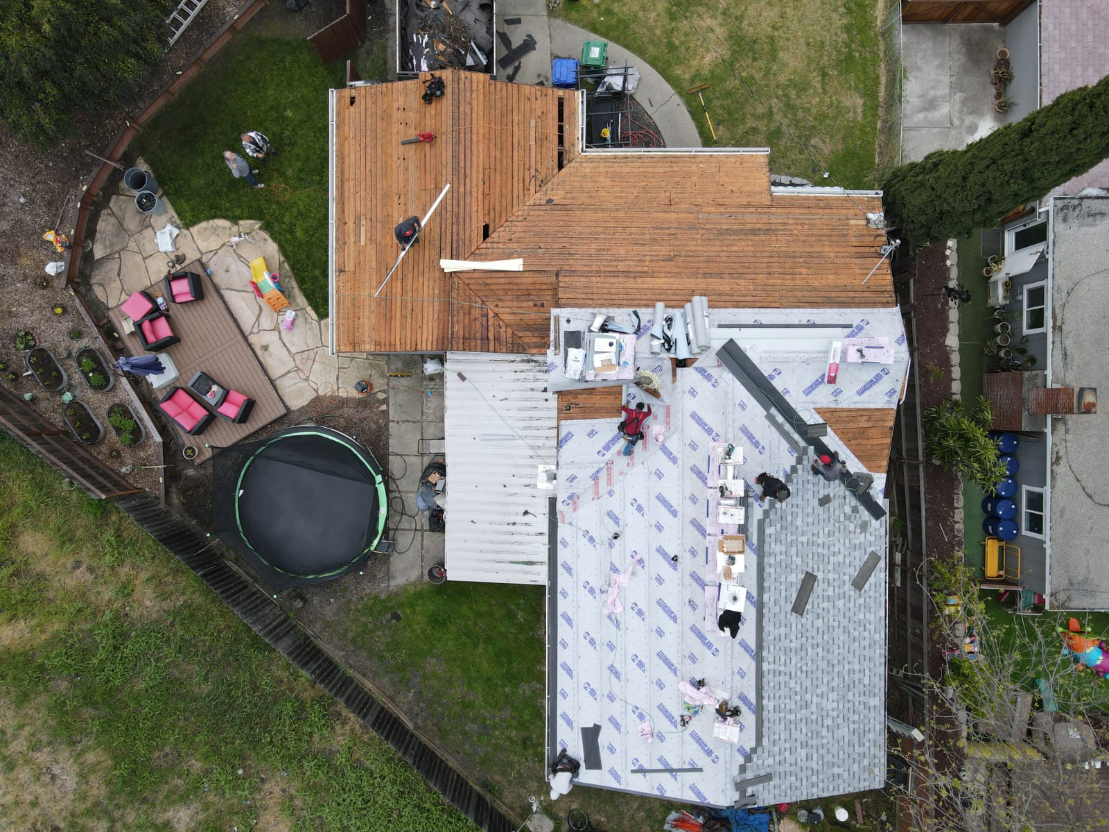 The image shows a residential house undergoing roof renovation, with visible construction materials such as plywood and insulation, and a partially completed deck attached to the second story.