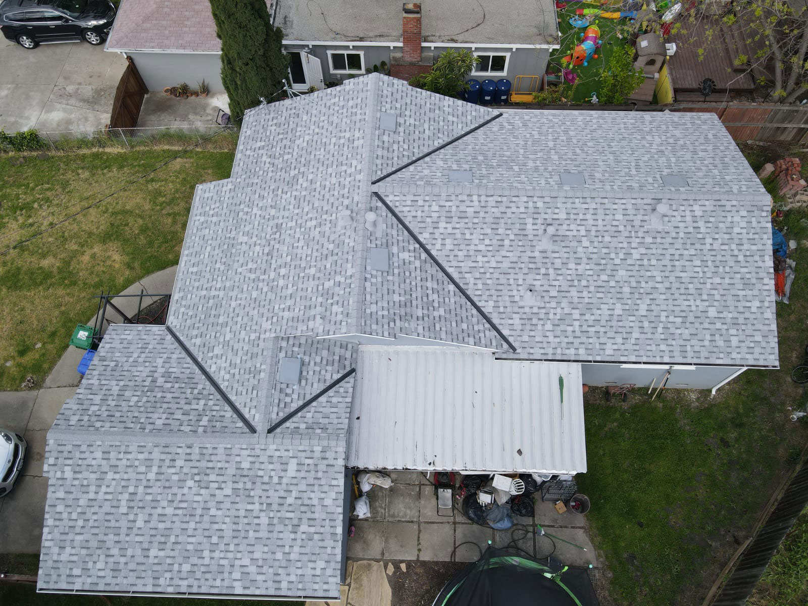 The image shows a house with a prominent gray metal roof and a visible shingle pattern underneath.