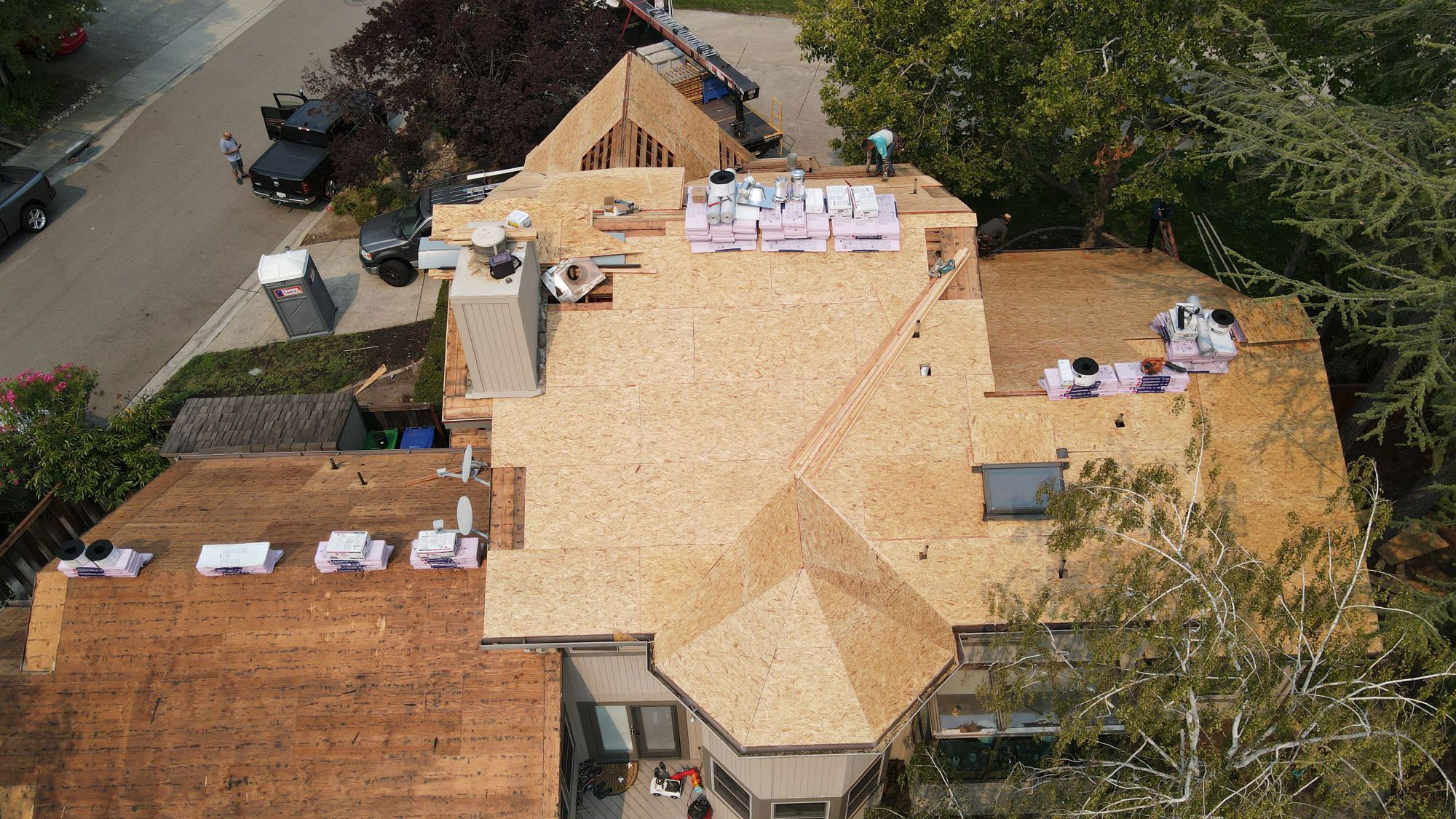 The image shows a house undergoing construction with visible wooden framing and roofing materials installed.