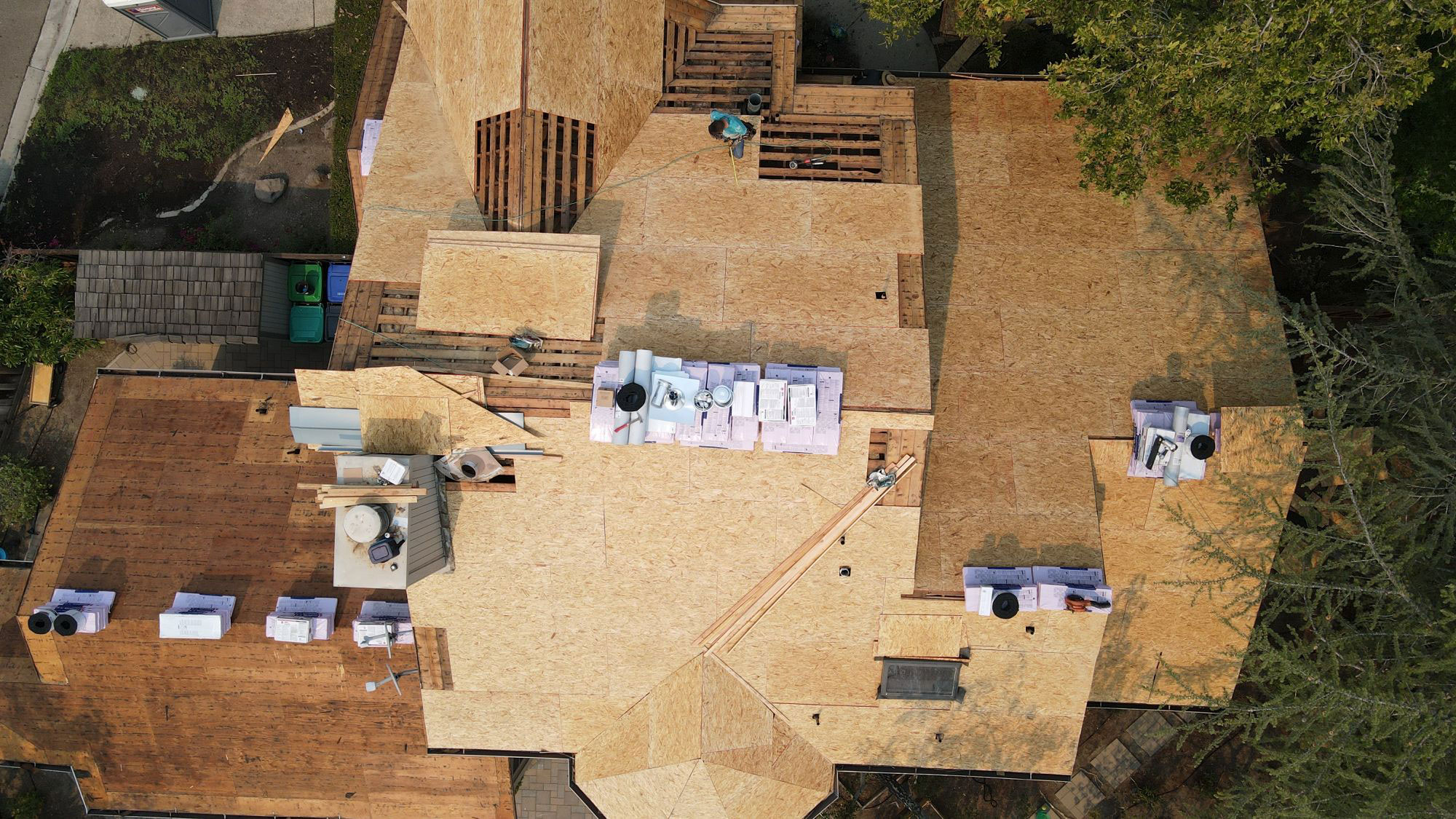 The image shows a house under construction with visible wooden framing and partially installed roofing materials.