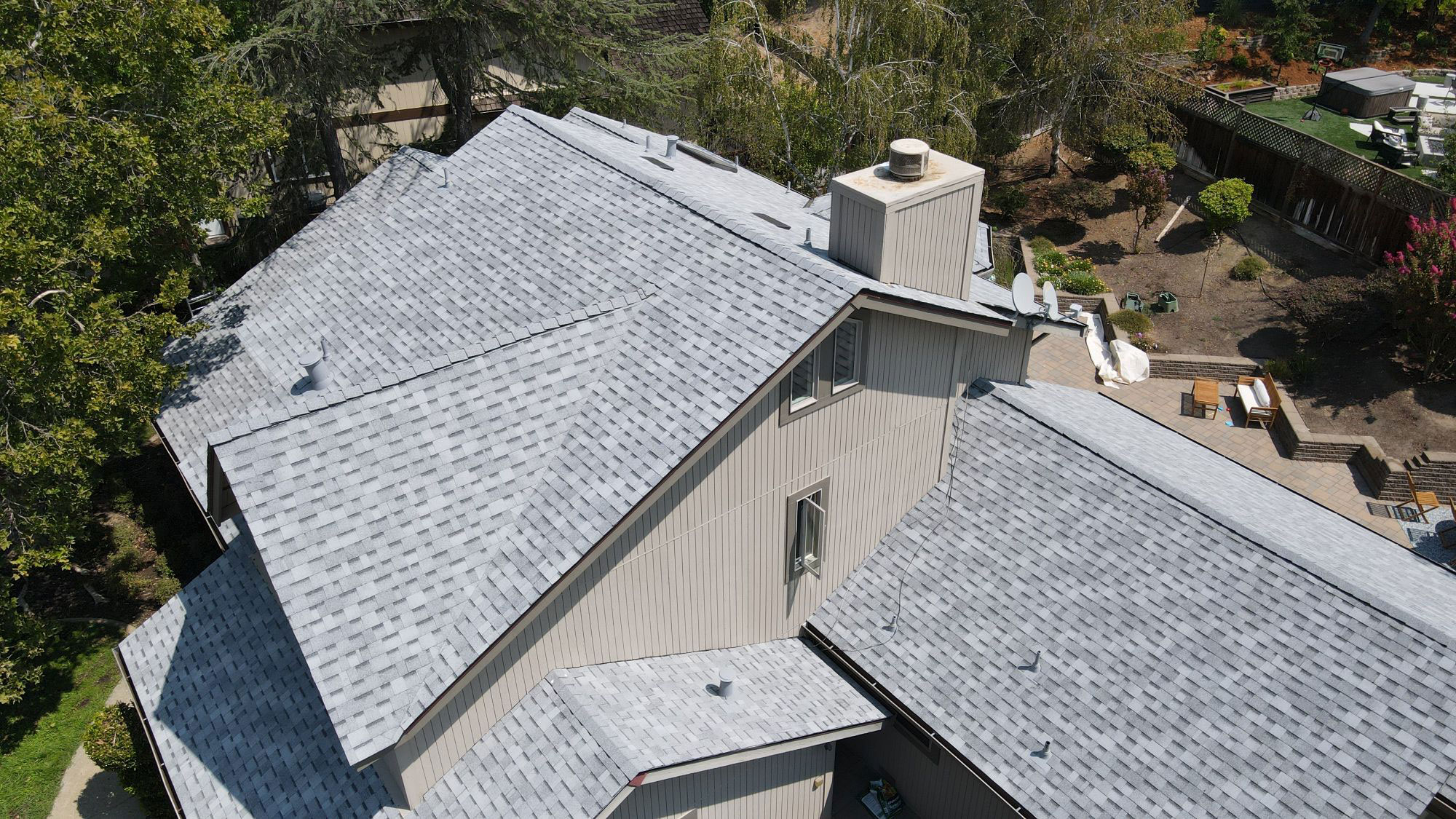 The image shows a residential house with a grey shingle roof under a clear sky.