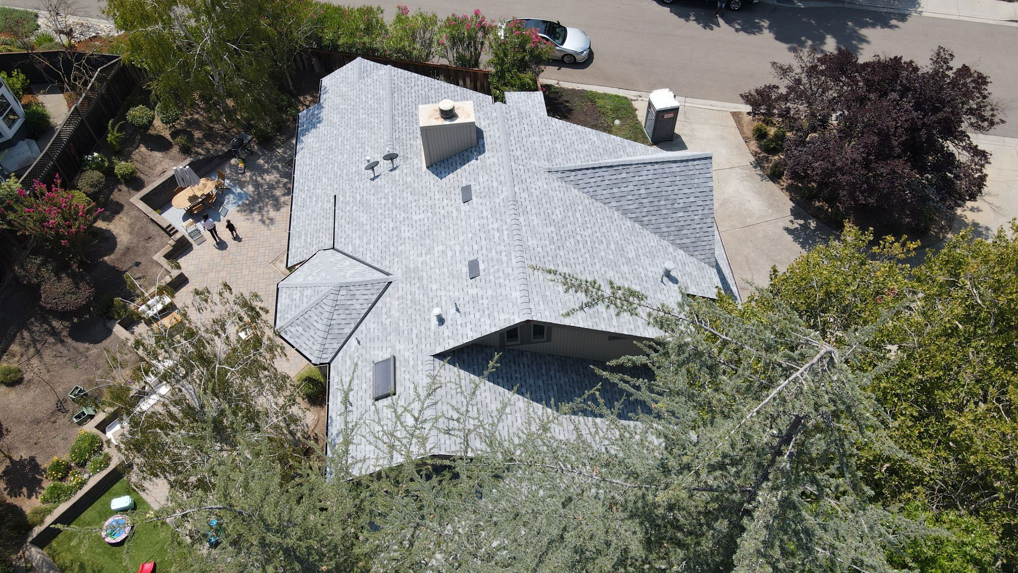 The image shows a house with a prominent roof extension featuring a peaked design, surrounded by landscaping and a clear sky.