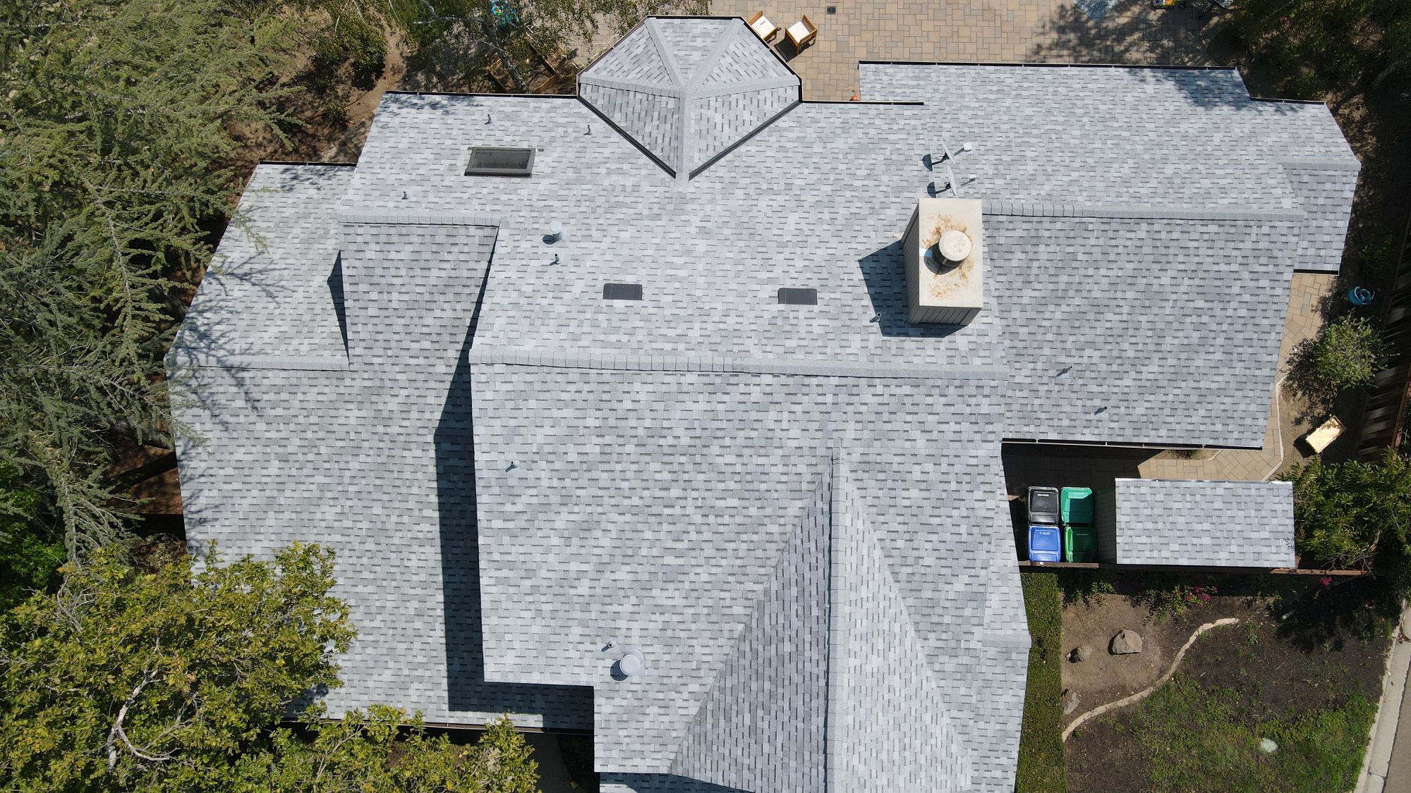 A large house with a grey tile roof under construction, viewed from an angle showing its architectural design.