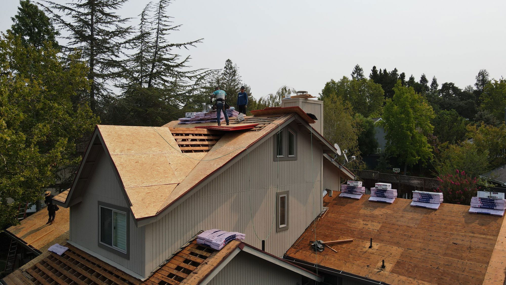 A house under construction with visible roofing materials and workers on the roof.