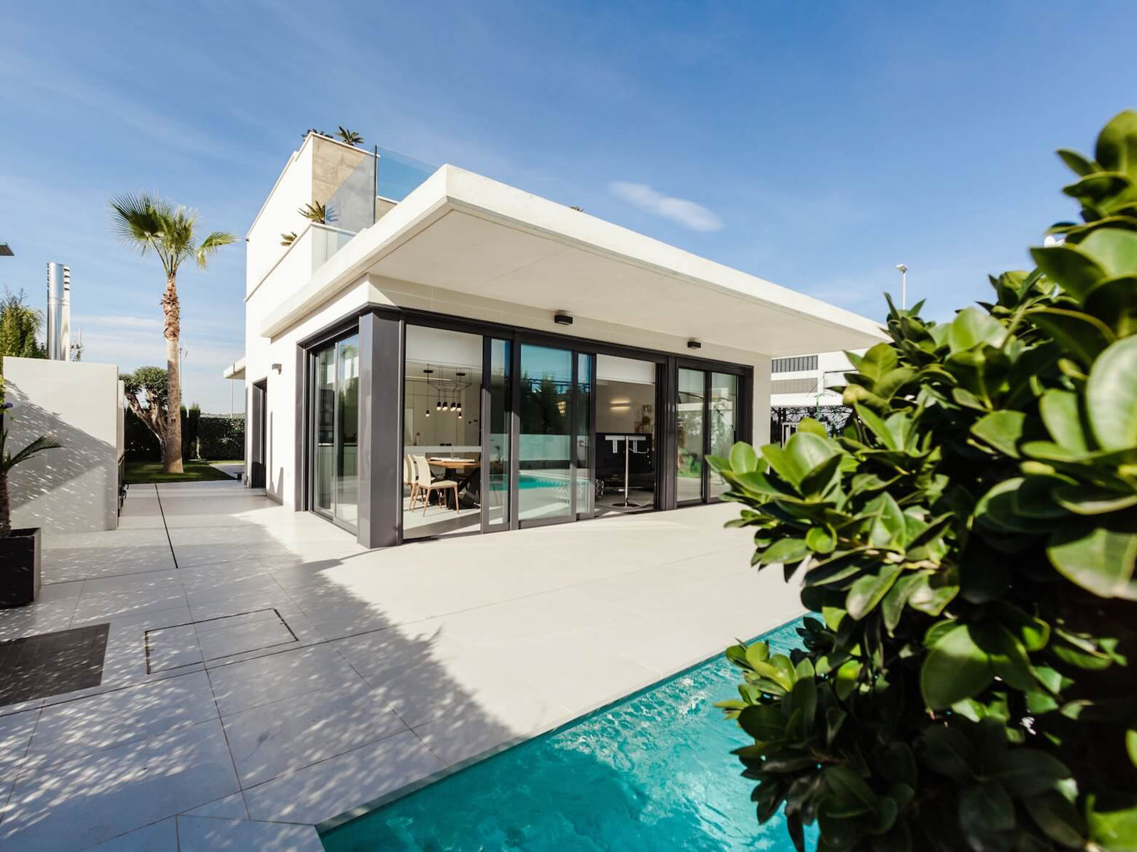A modern single-story house with a pool and palm trees against a clear sky.