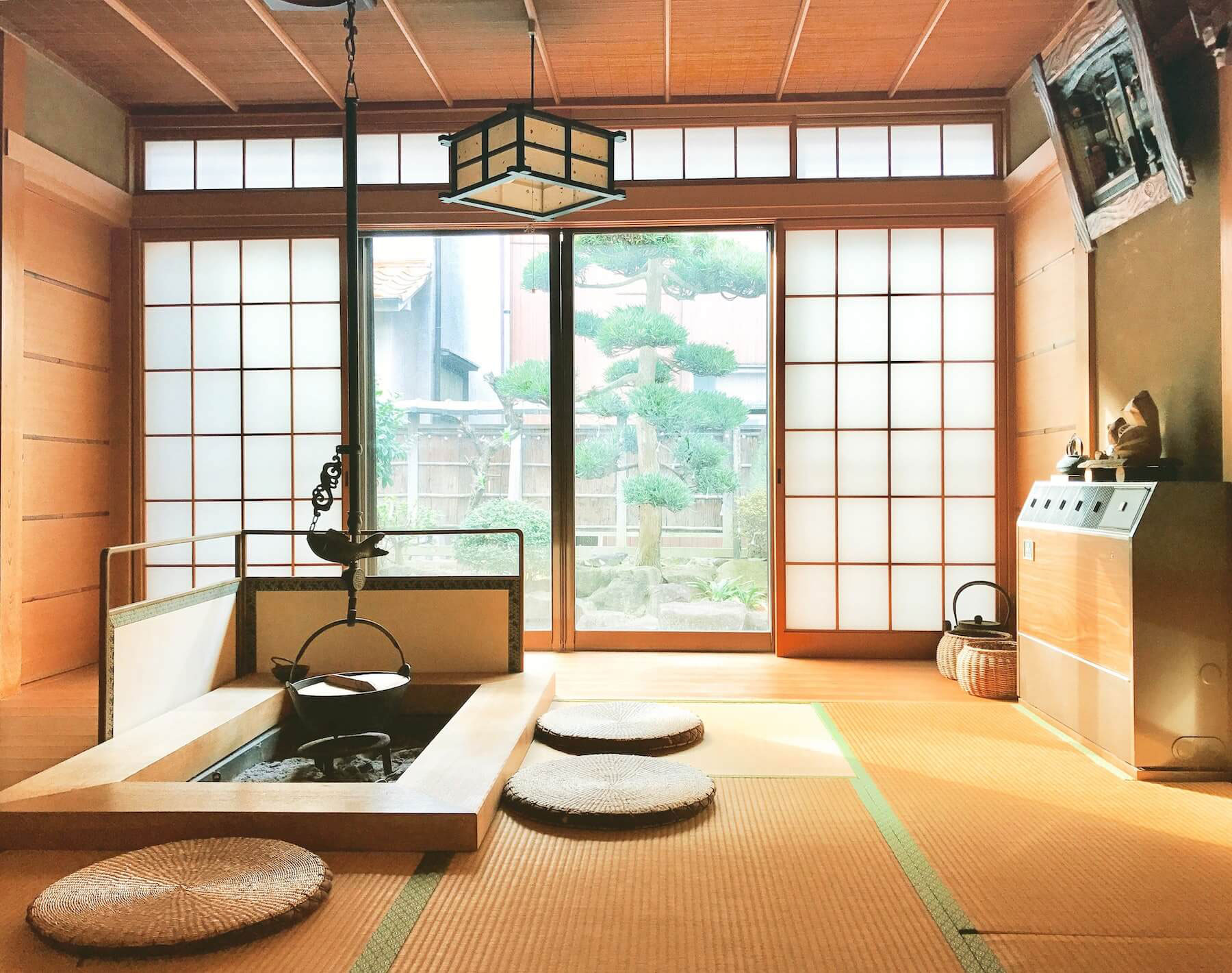 A traditional Japanese room with tatami flooring, a tea set, and a soaking tub in the foreground, illuminated by natural light from large windows.
