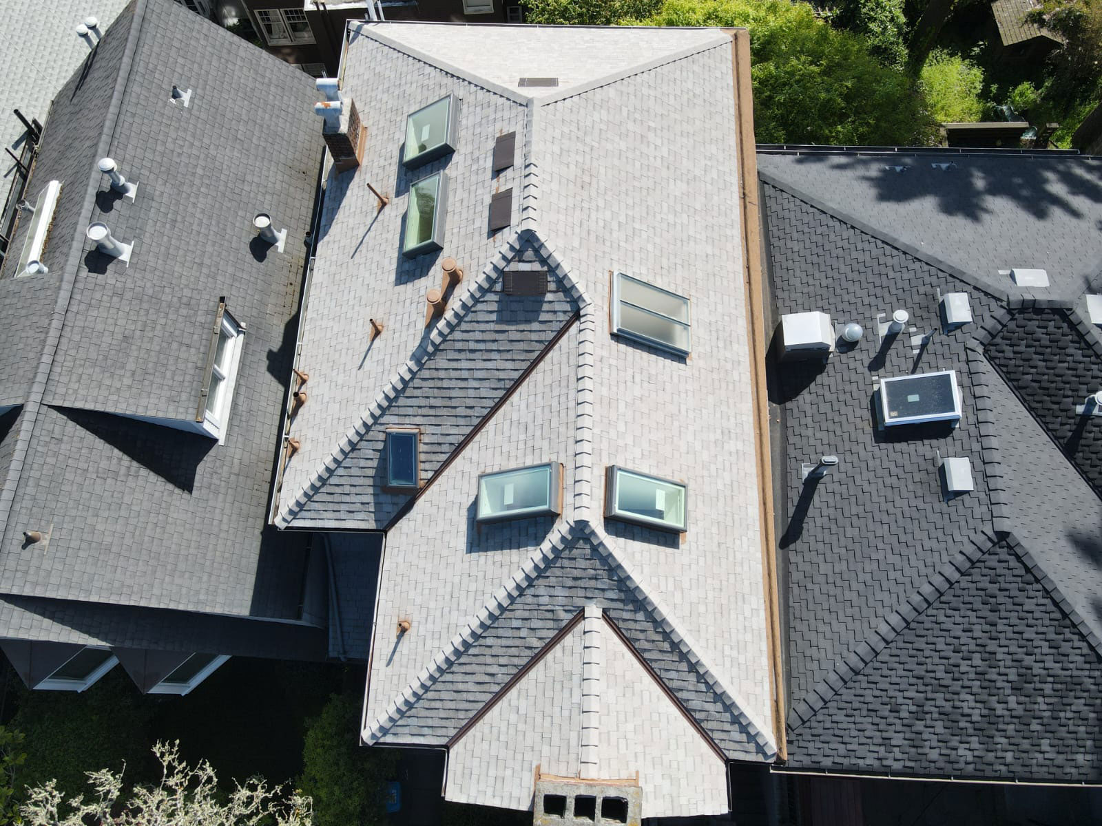 A photograph of a residential house with a pitched roof featuring multiple skylights, an extended eave, and a sunroof over a central section. The house has a shingled exterior and appears to be in an urban setting.
