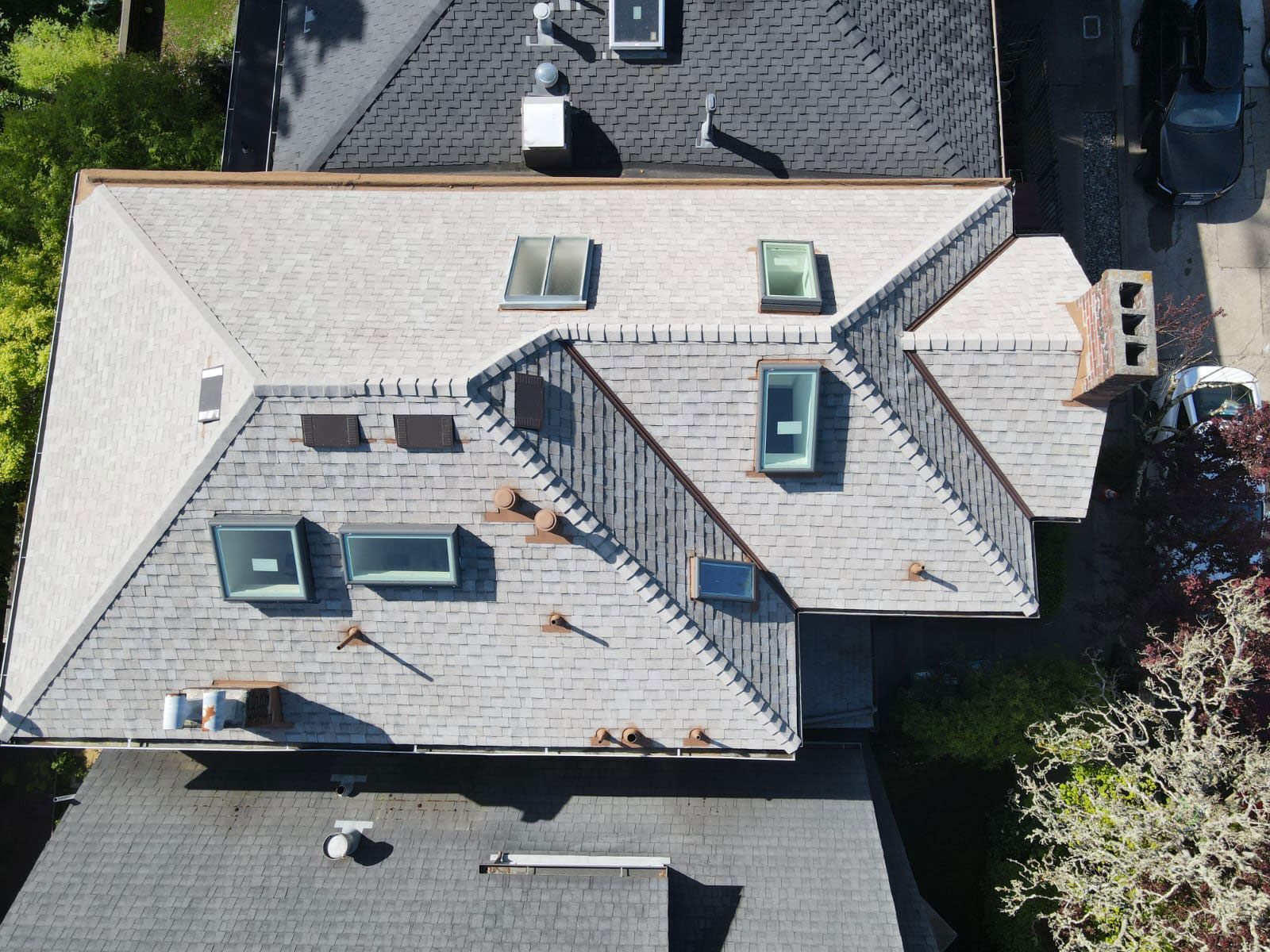 The image shows a residential house with a gray shingled roof, multiple skylights, and a prominent triangular dormer window.