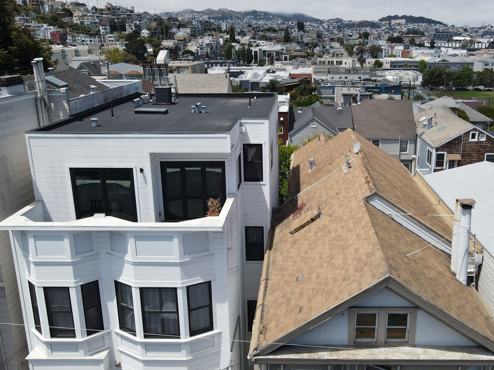 The image shows a row of modern two-story residential buildings with white exteriors, black roofs, and balconies, situated side by side on a street with a clear sky above.