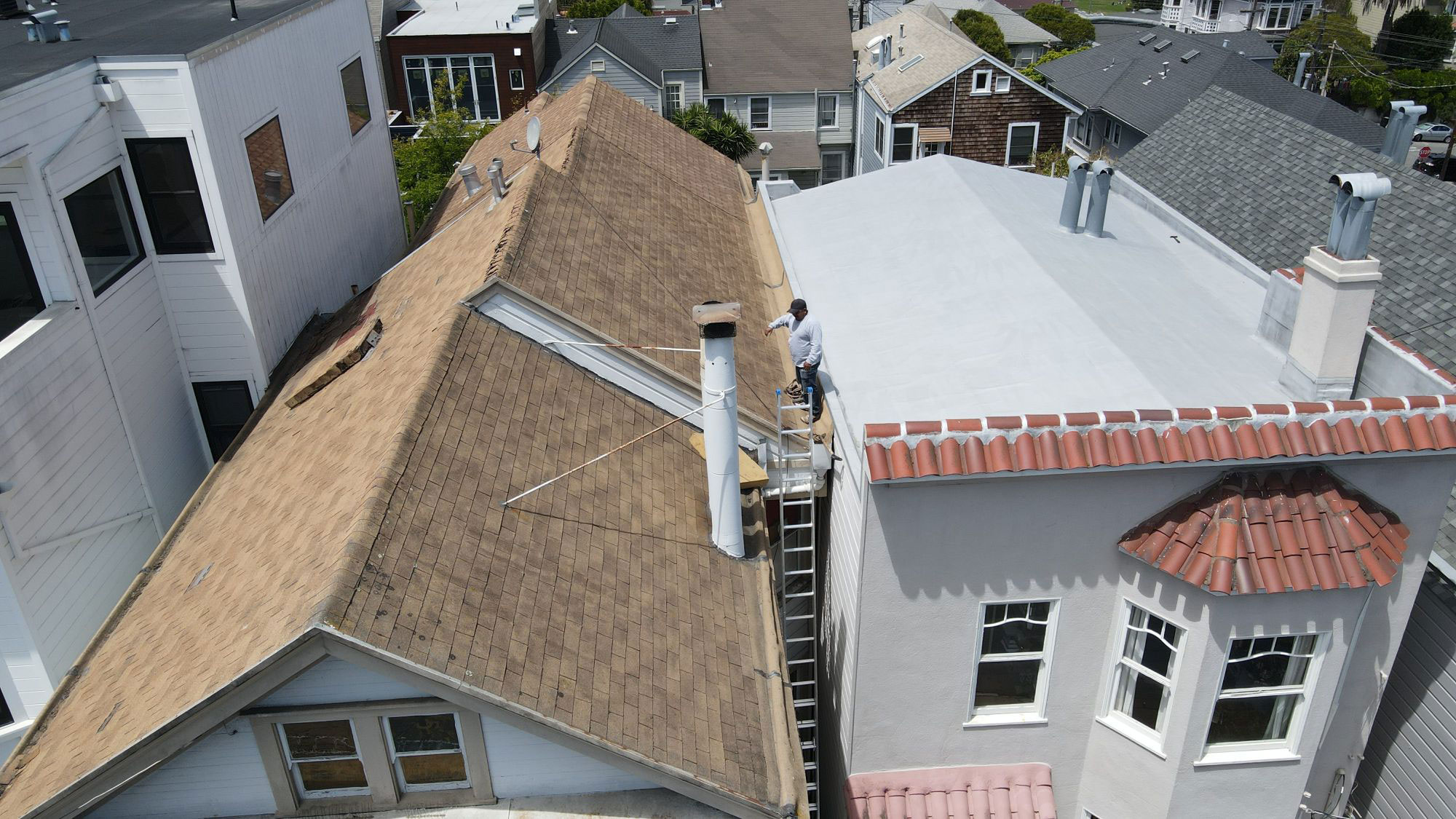 The image shows a residential street scene with houses under construction or renovation, featuring exposed roofs and exterior work in progress.