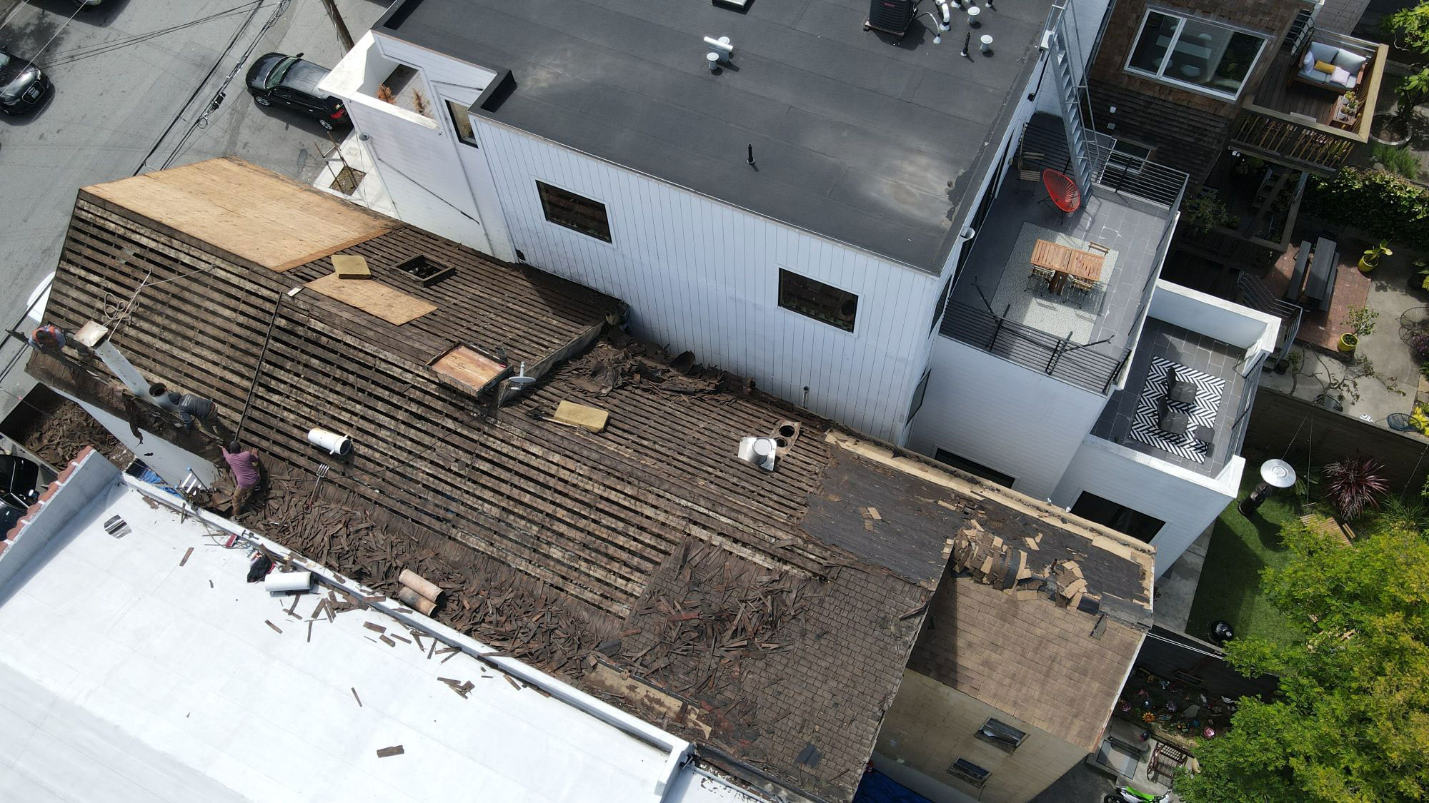 The image shows a building with a damaged roof, undergoing renovation or repair, with visible construction materials and debris on the ground.