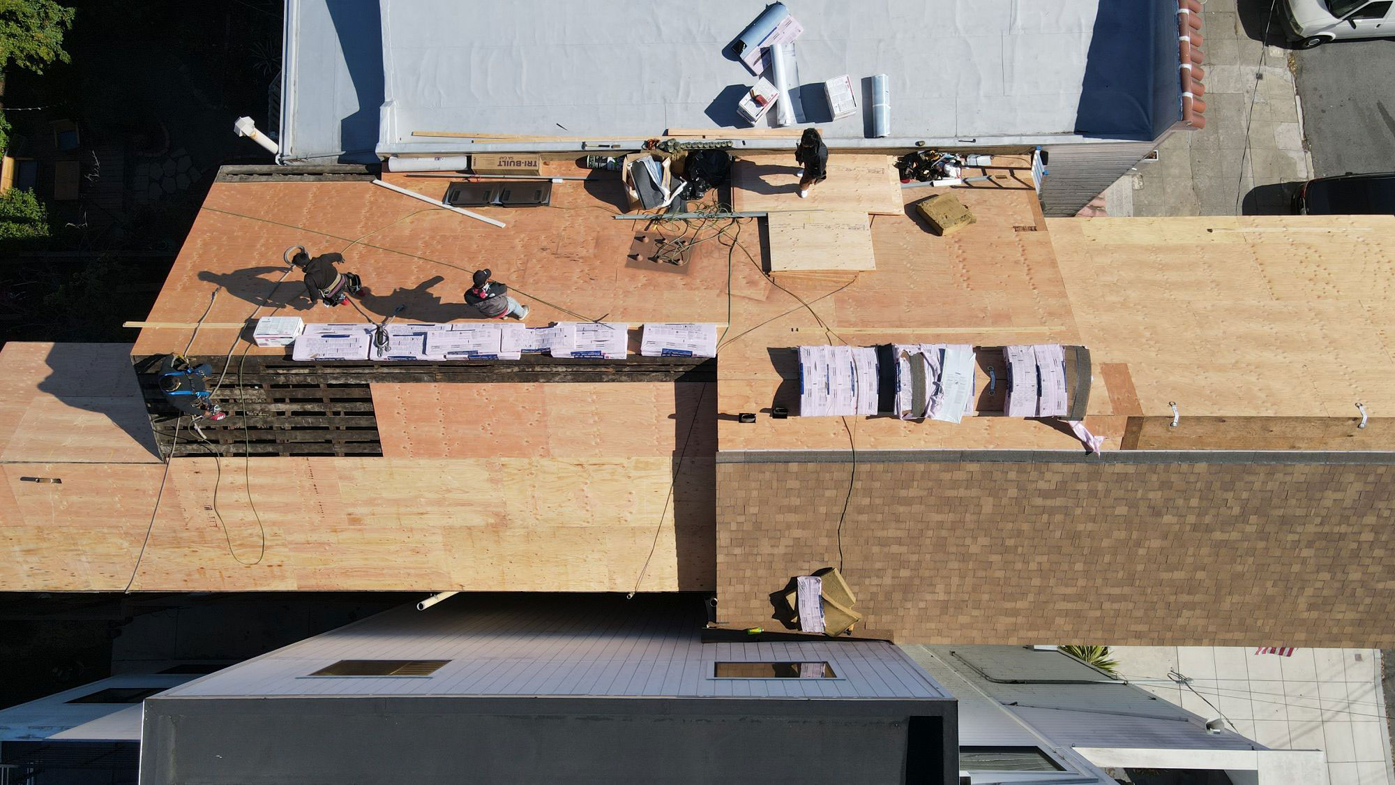 The image shows a building under construction with a visible wooden roof structure, scaffolding, and various materials on the ground.