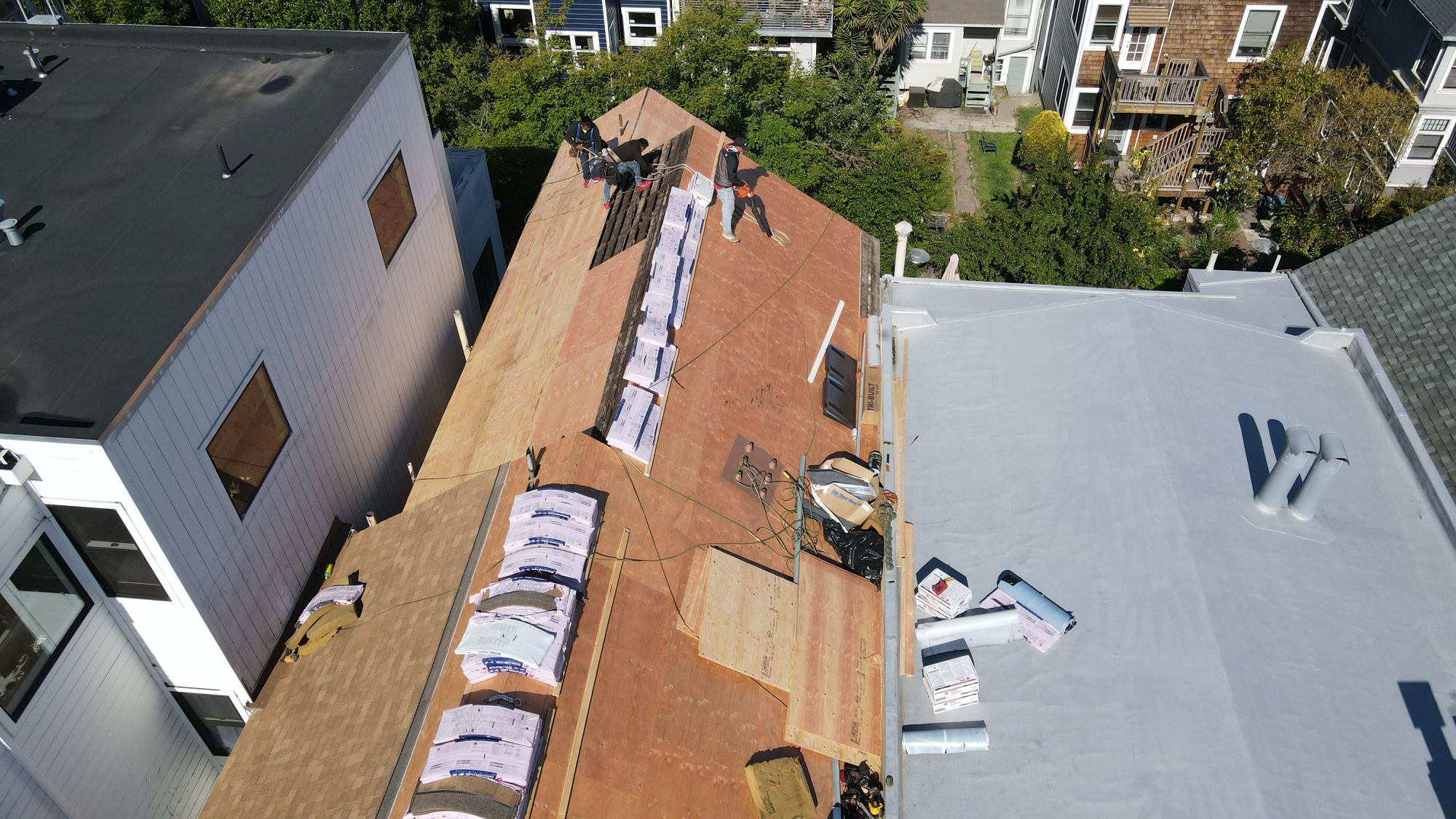 The image shows a residential rooftop under construction, with visible materials such as plywood and insulation, and a partially completed structure in the foreground.