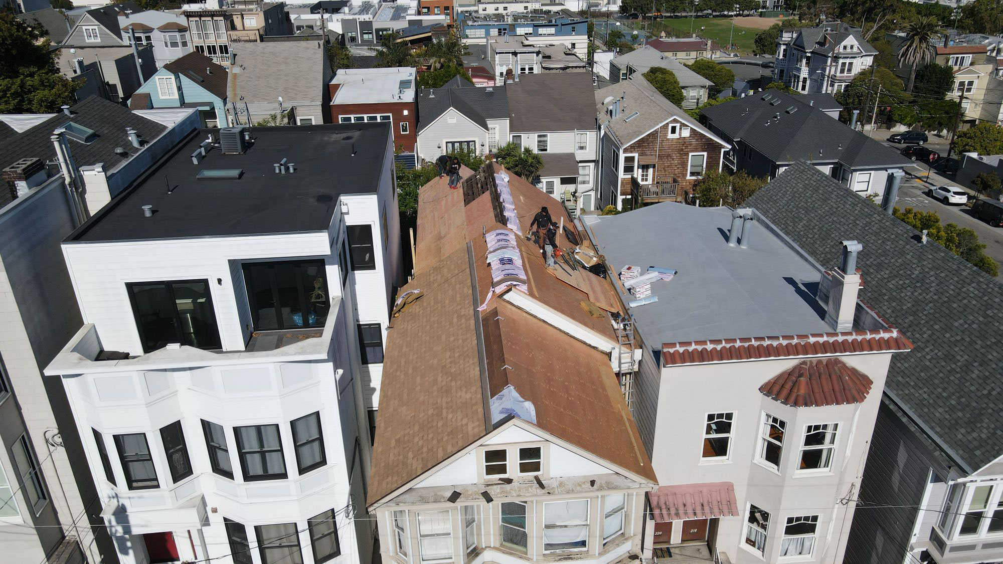 The image shows a residential street scene with multi-story houses under construction, featuring visible roofs and exterior walls, set against a clear sky.