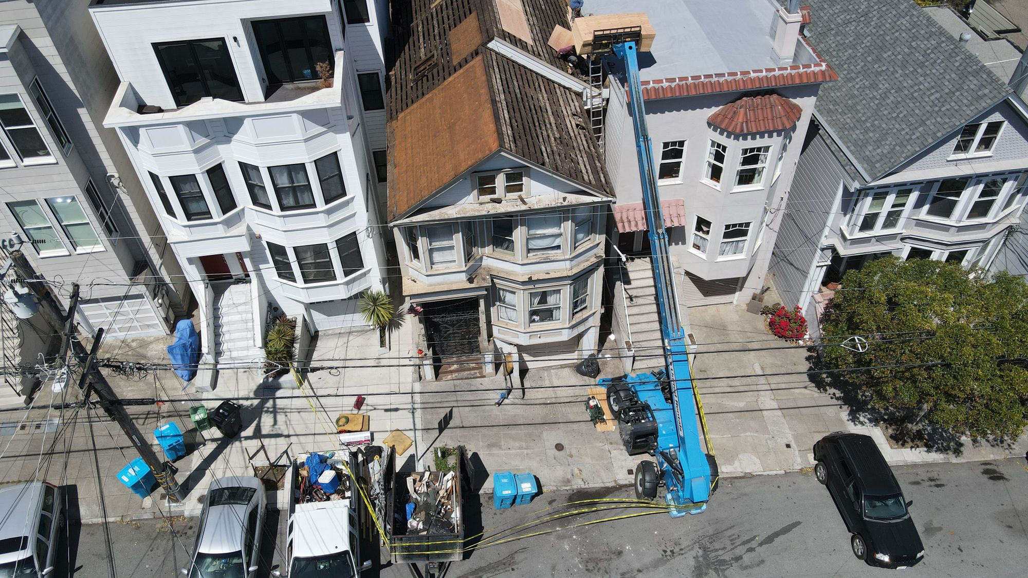 The image shows a residential street scene with a two-story house under construction or renovation, featuring scaffolding and workers at the site.