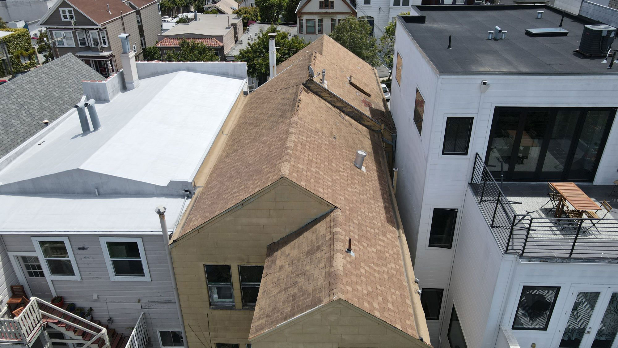 The image shows a row of houses with flat roofs, with one house featuring an extended roofline and a prominent skylight.