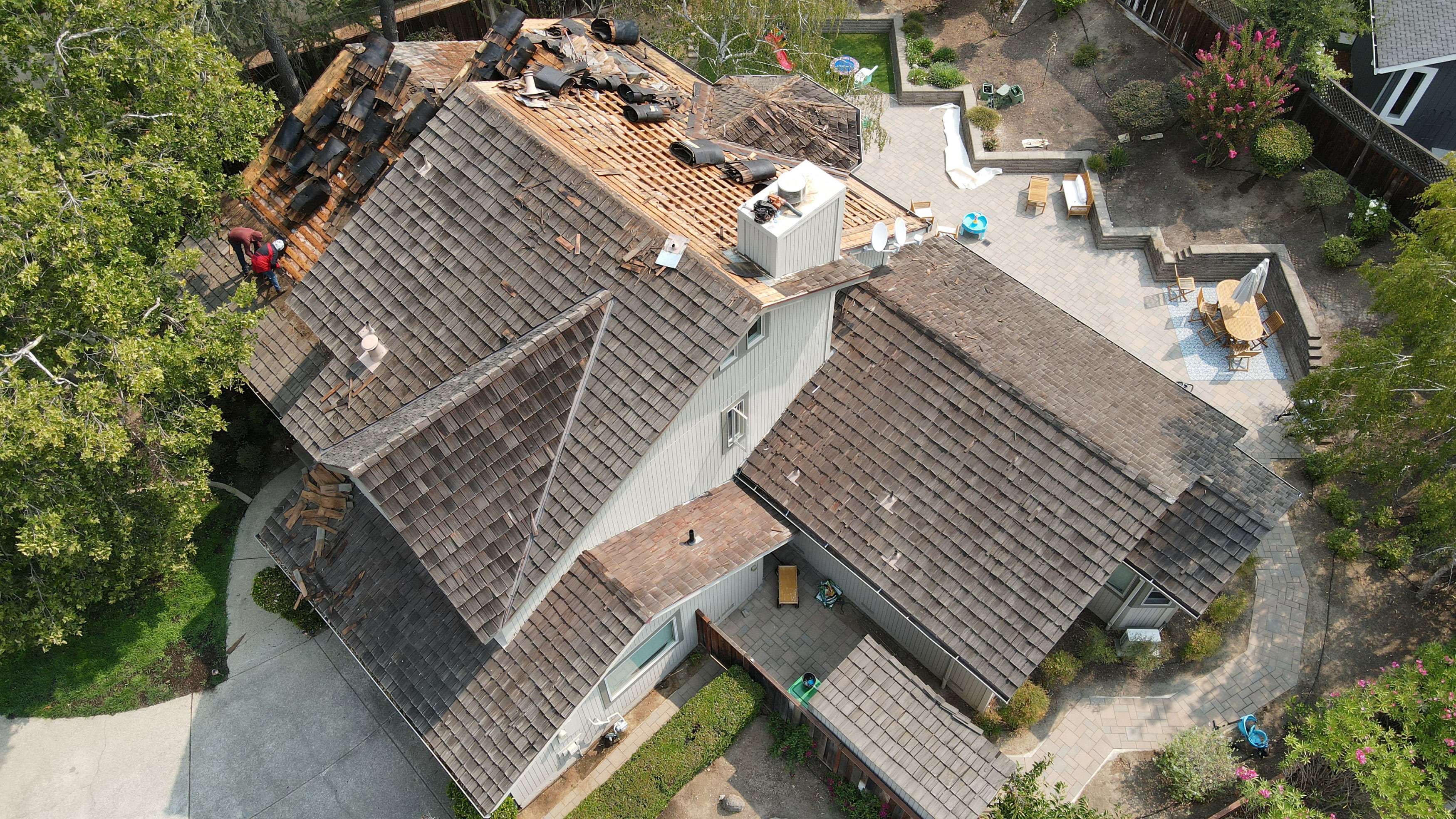 The image shows a residential house with visible roof damage, undergoing repairs, with construction materials on the ground outside.