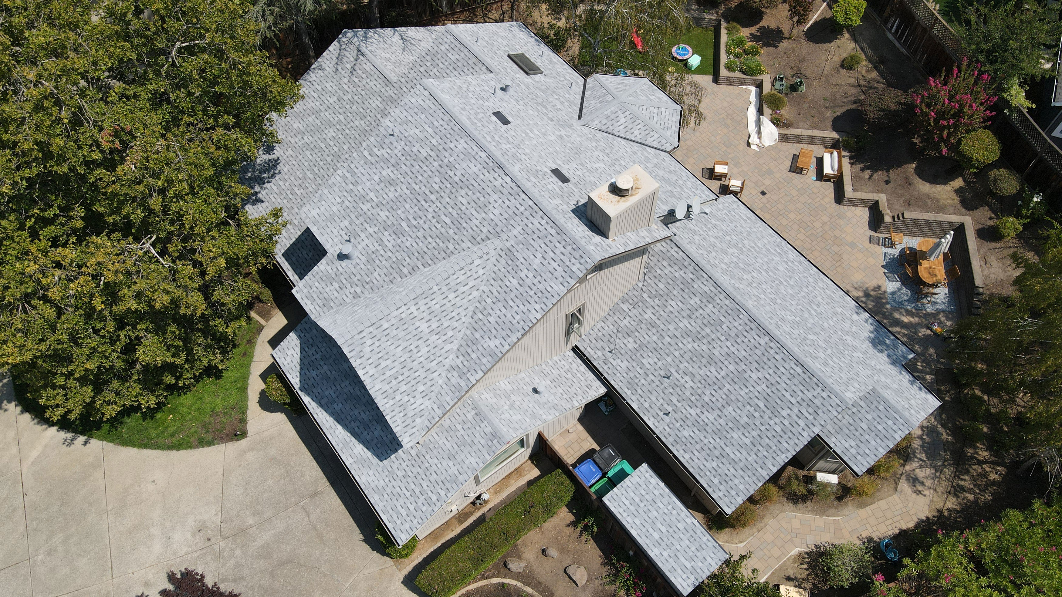The image shows a large, two-story residential house with an unusual, irregular roofline featuring multiple slopes and angles, set against a clear sky.