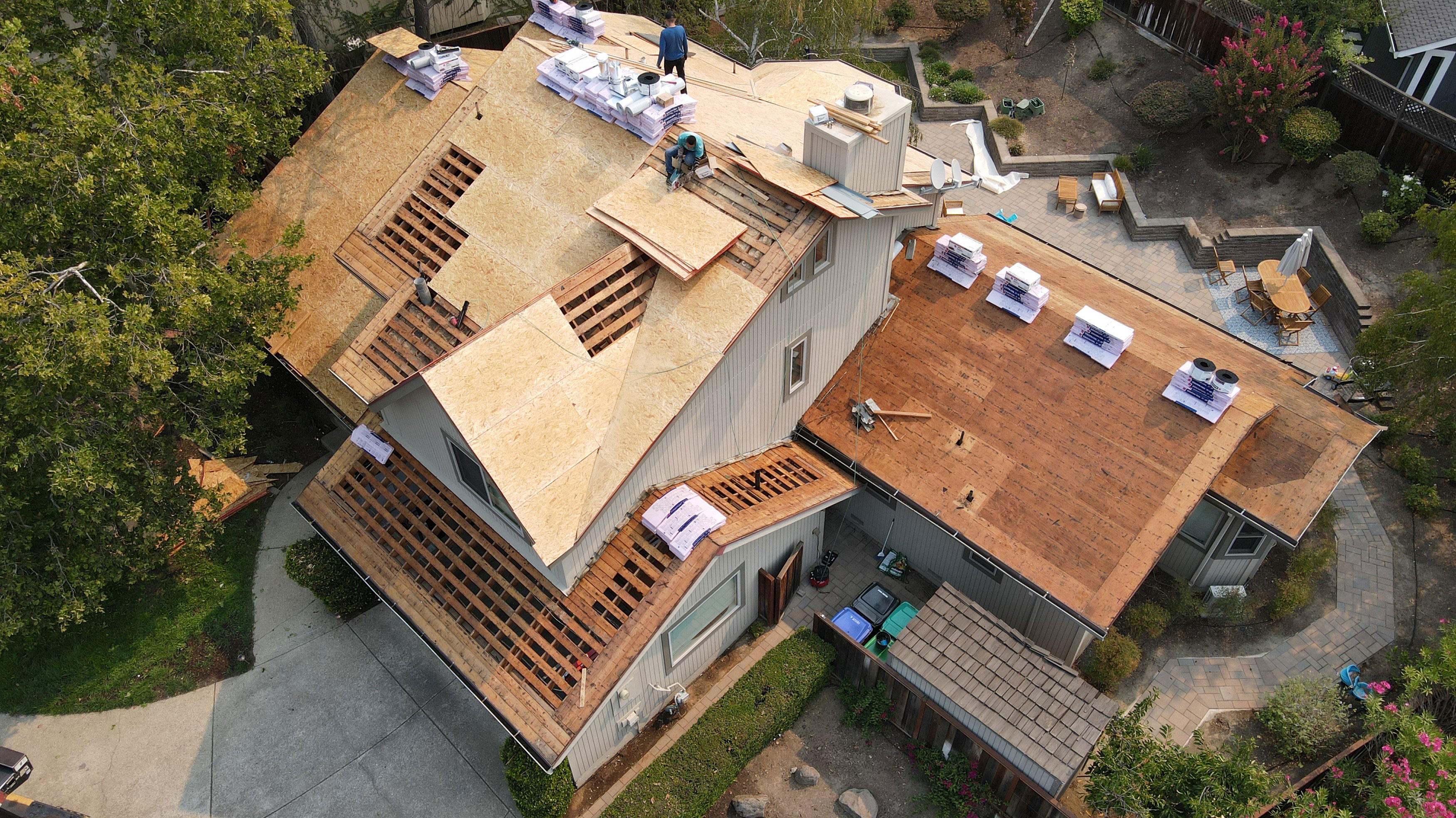 This image shows a house under construction with visible roofing materials and tools on the ground around it.