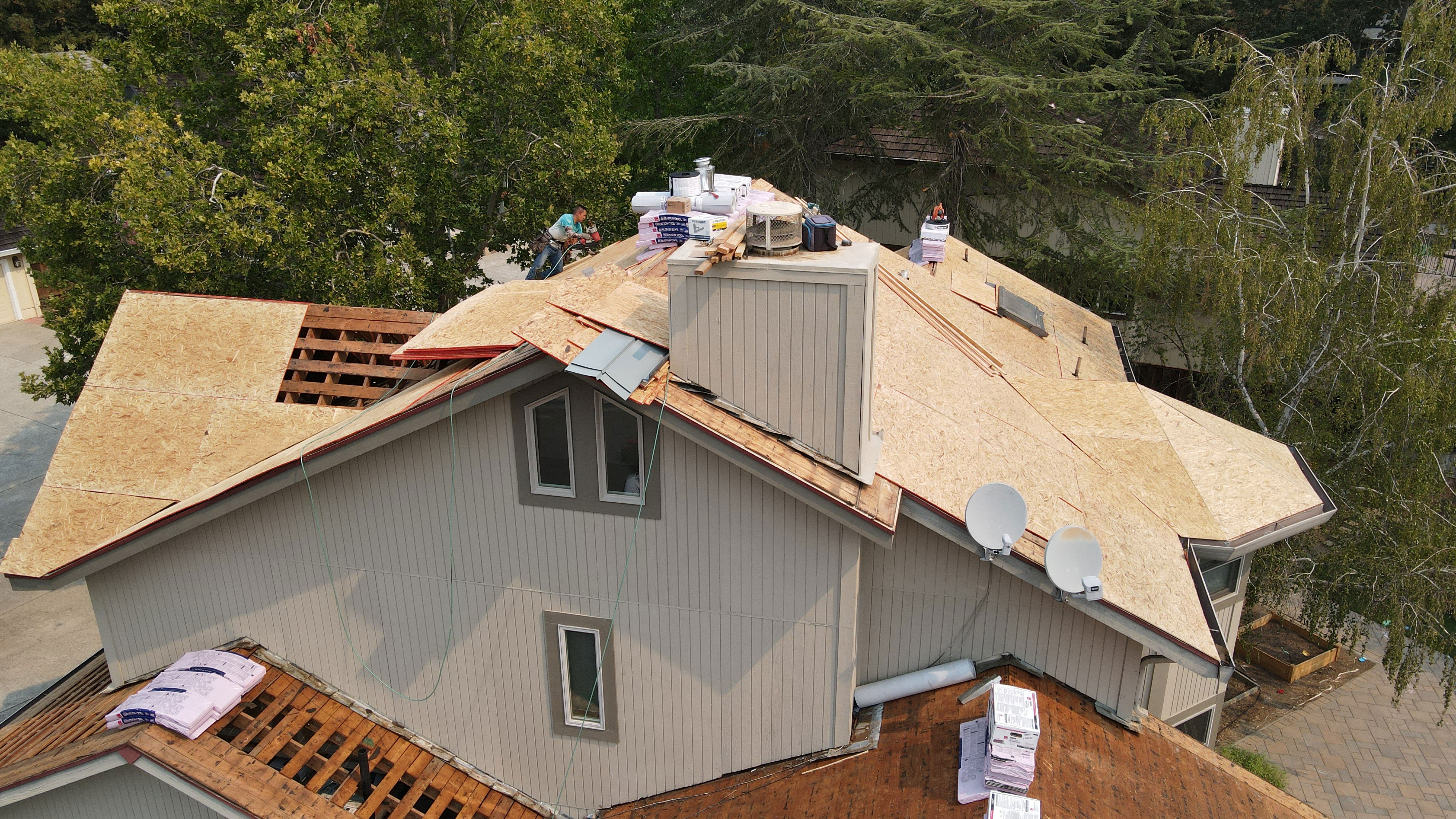The image shows a house with a partially completed roof, featuring exposed wooden rafters and a visible patch where shingles have been removed or replaced.