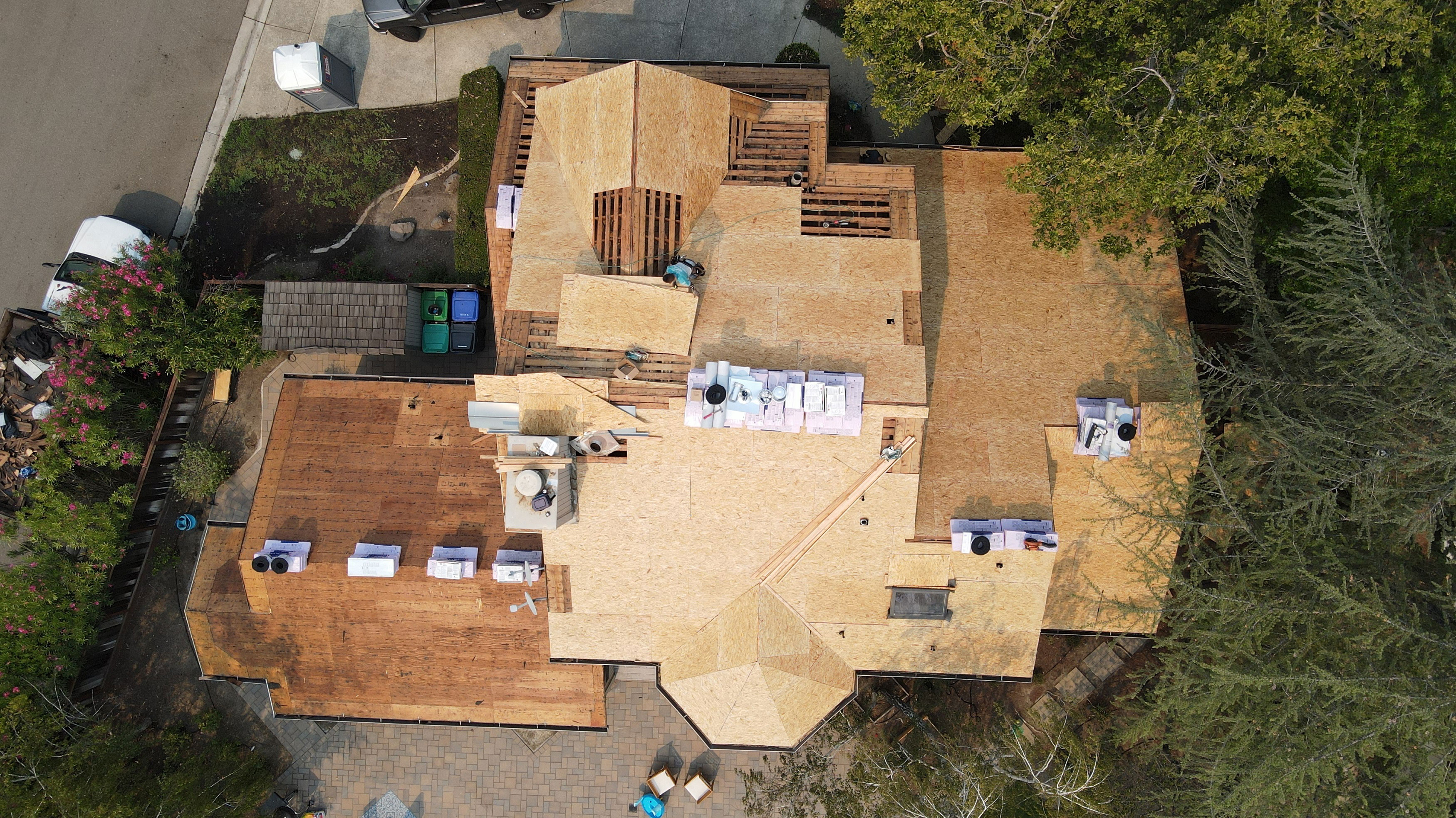 The image shows a house under construction with visible wooden framing, roofing materials, and some exterior finishes being applied.