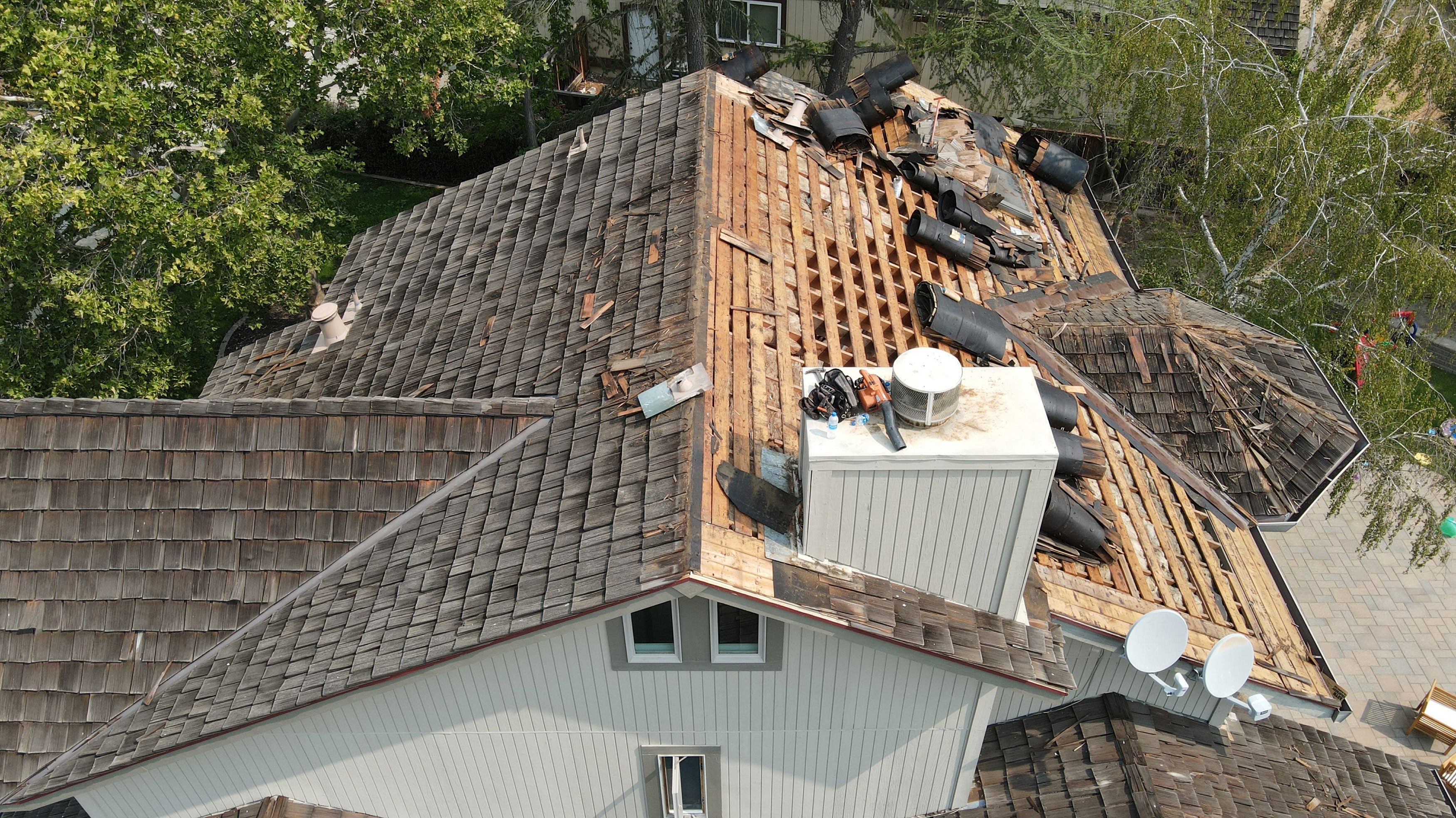 The image shows a house with a damaged roof undergoing repair; there are visible tarps and exposed wooden decking on the upper level, indicating ongoing construction work.