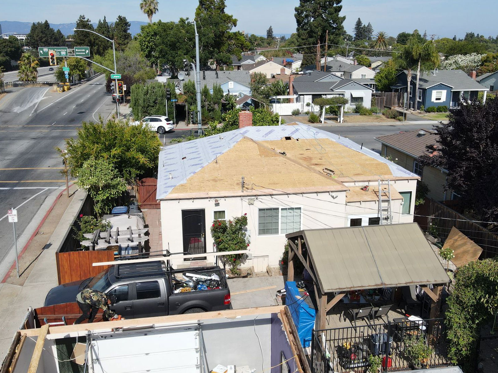 The image shows a residential area with a house undergoing roof construction, surrounded by various vehicles parked nearby.