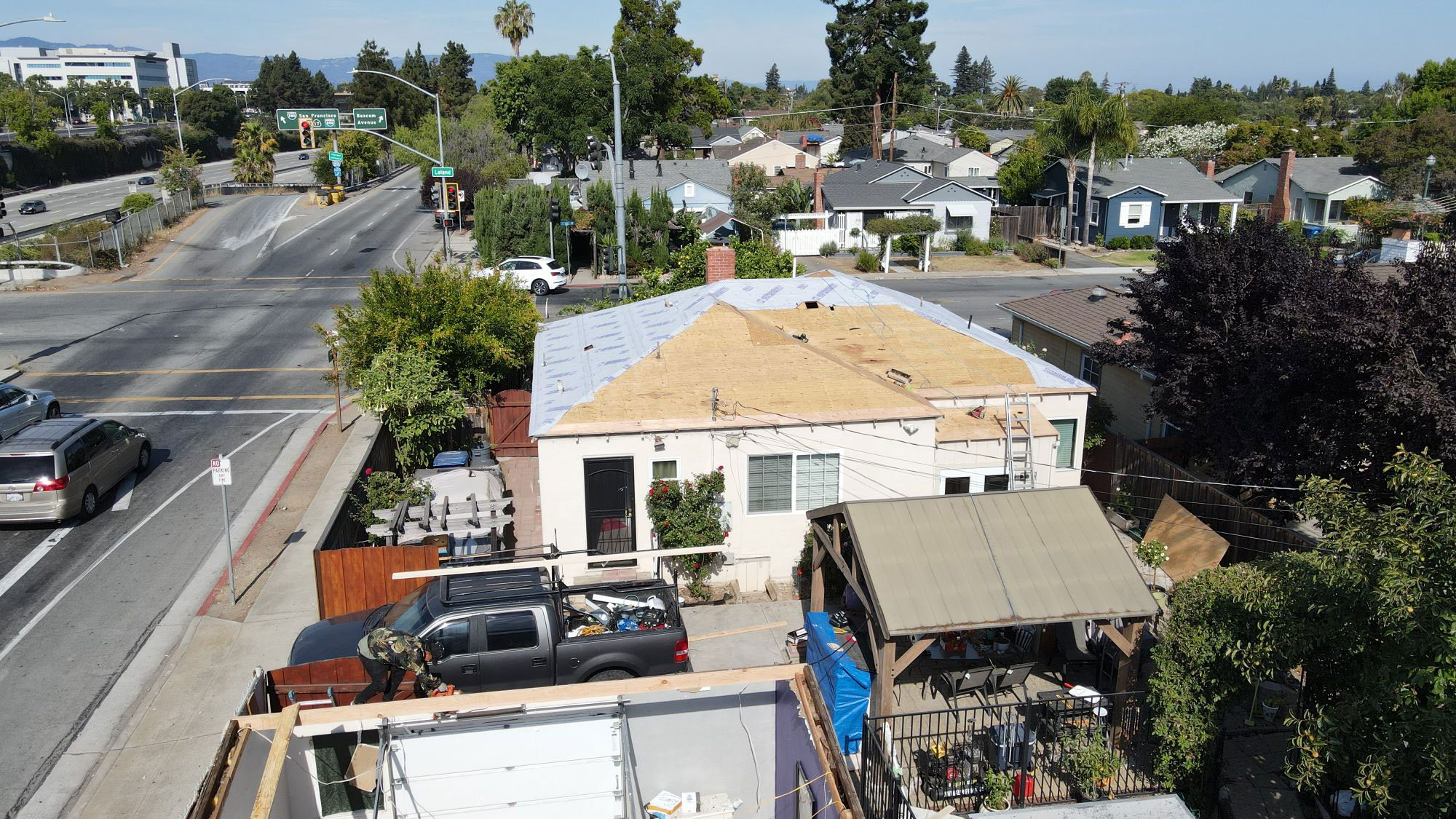 The image shows a residential street scene with a house under construction or renovation, visible from an elevated angle.