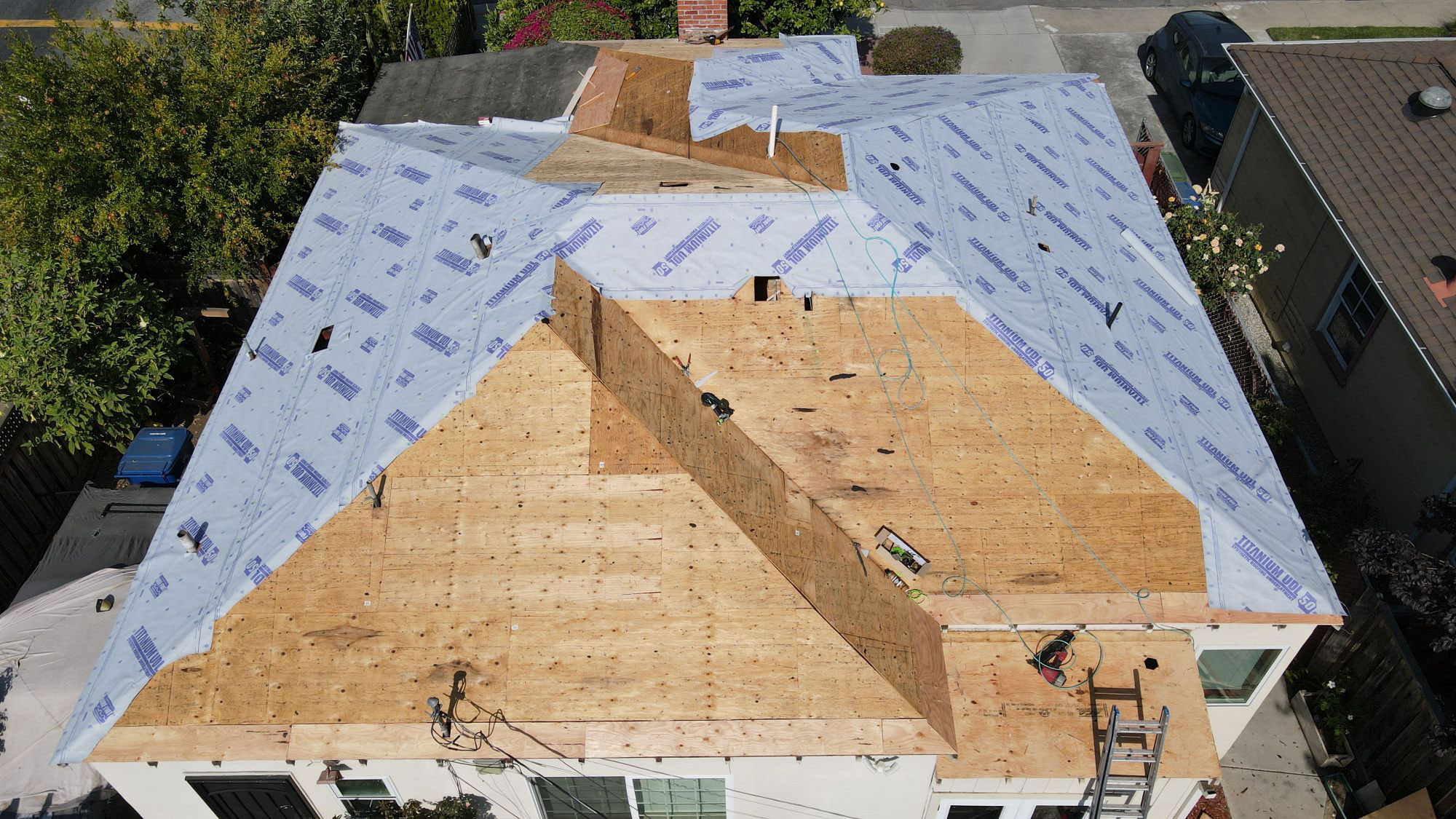 The image shows a house under construction with a visible roofing project in progress, featuring tarps covering certain areas of the roof.