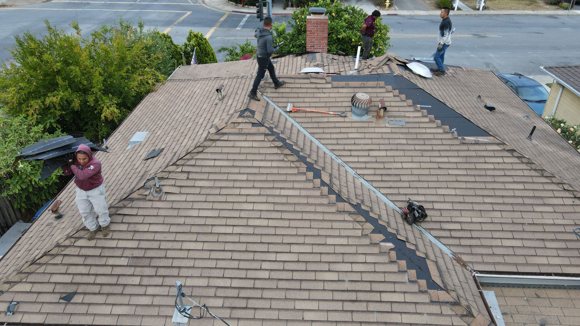 The image shows a roofing crew working on a residential house s roof, with various tools and materials visible during the construction process.