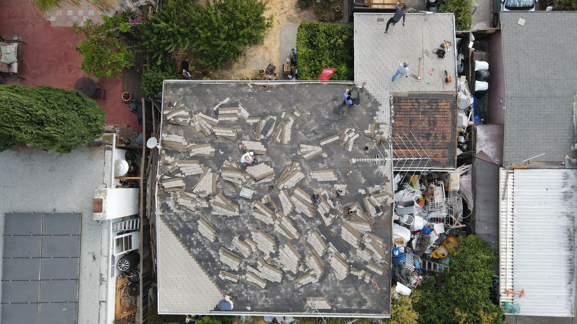 The image shows a roofing project underway on a residential building with various materials and tools scattered around the area, indicating ongoing construction work.