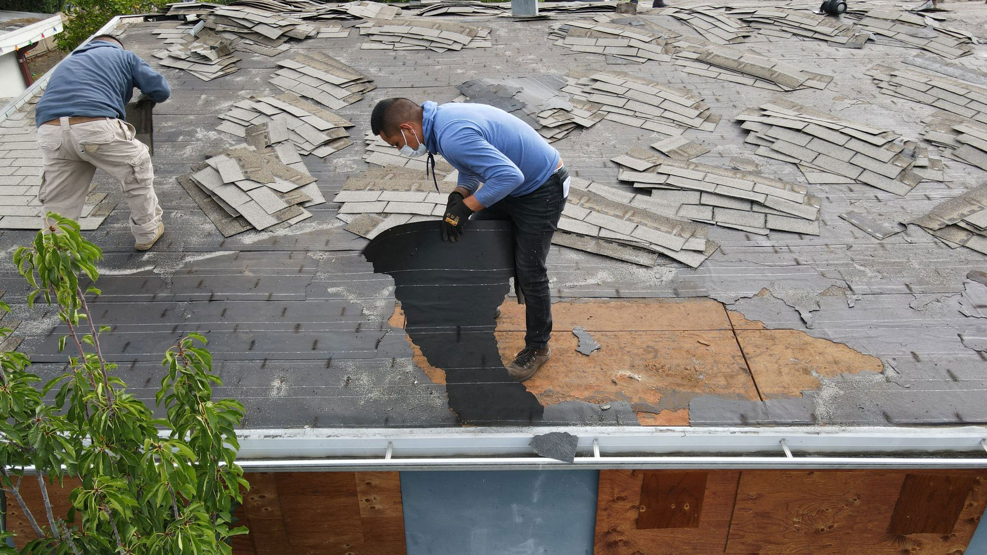 A person working on a roof repair with shingles removed, surrounded by construction materials.