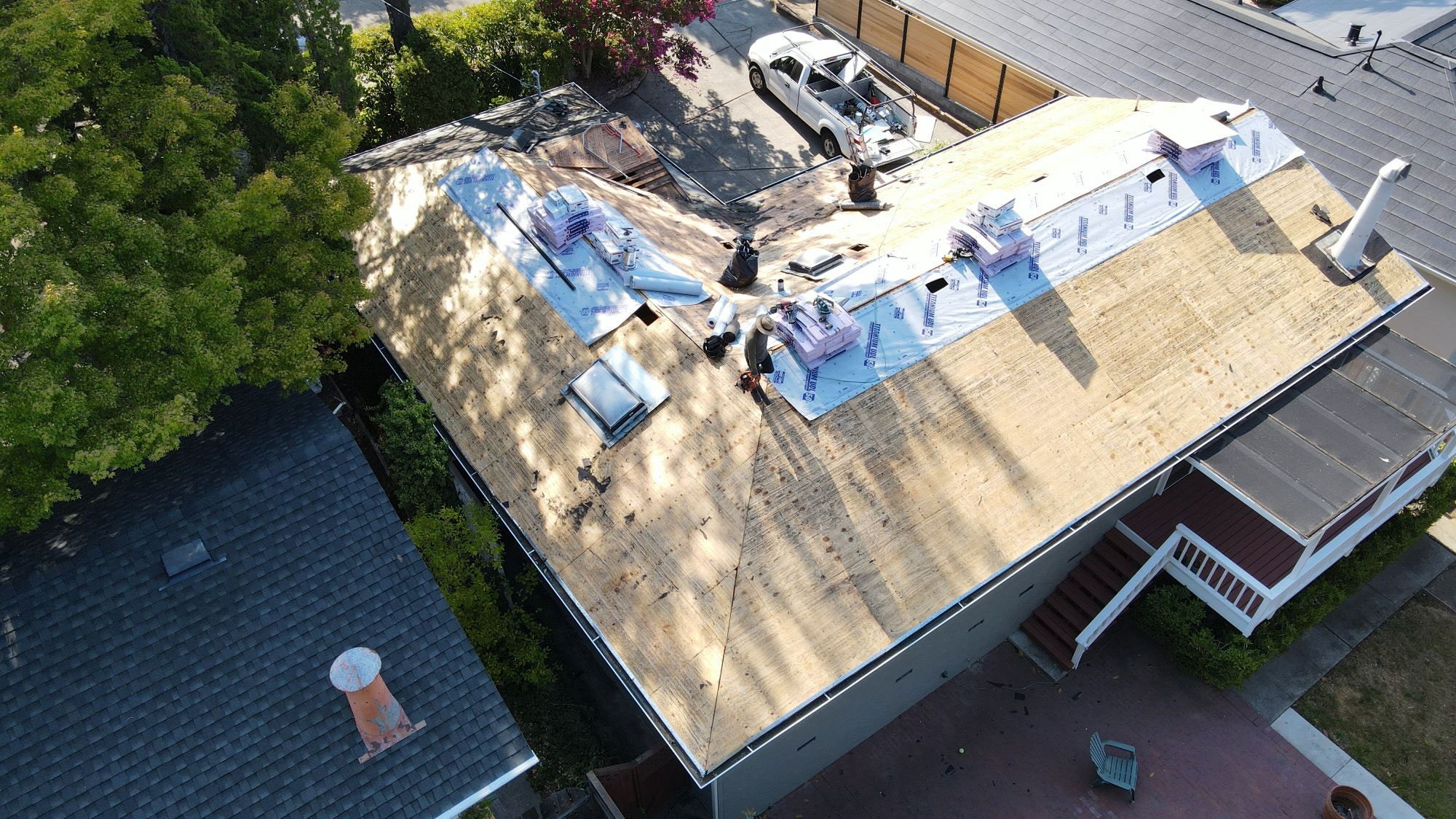 The image shows a residential building with a visible roof under construction or renovation, featuring exposed insulation materials and a partially installed new roof section.