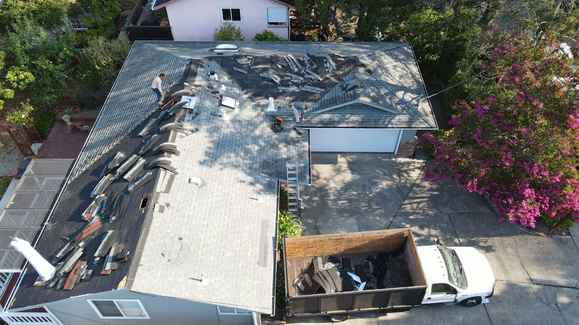 The image shows a house with a damaged roof, undergoing repair work, with debris scattered on the ground around it.