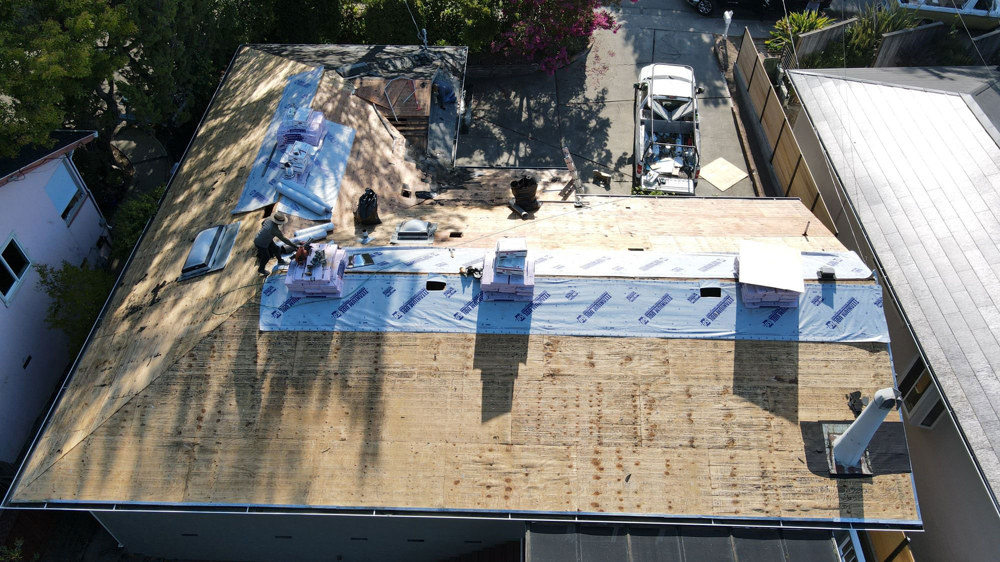 The image shows a roof under construction with visible tarps, indicating ongoing work on a residential building.